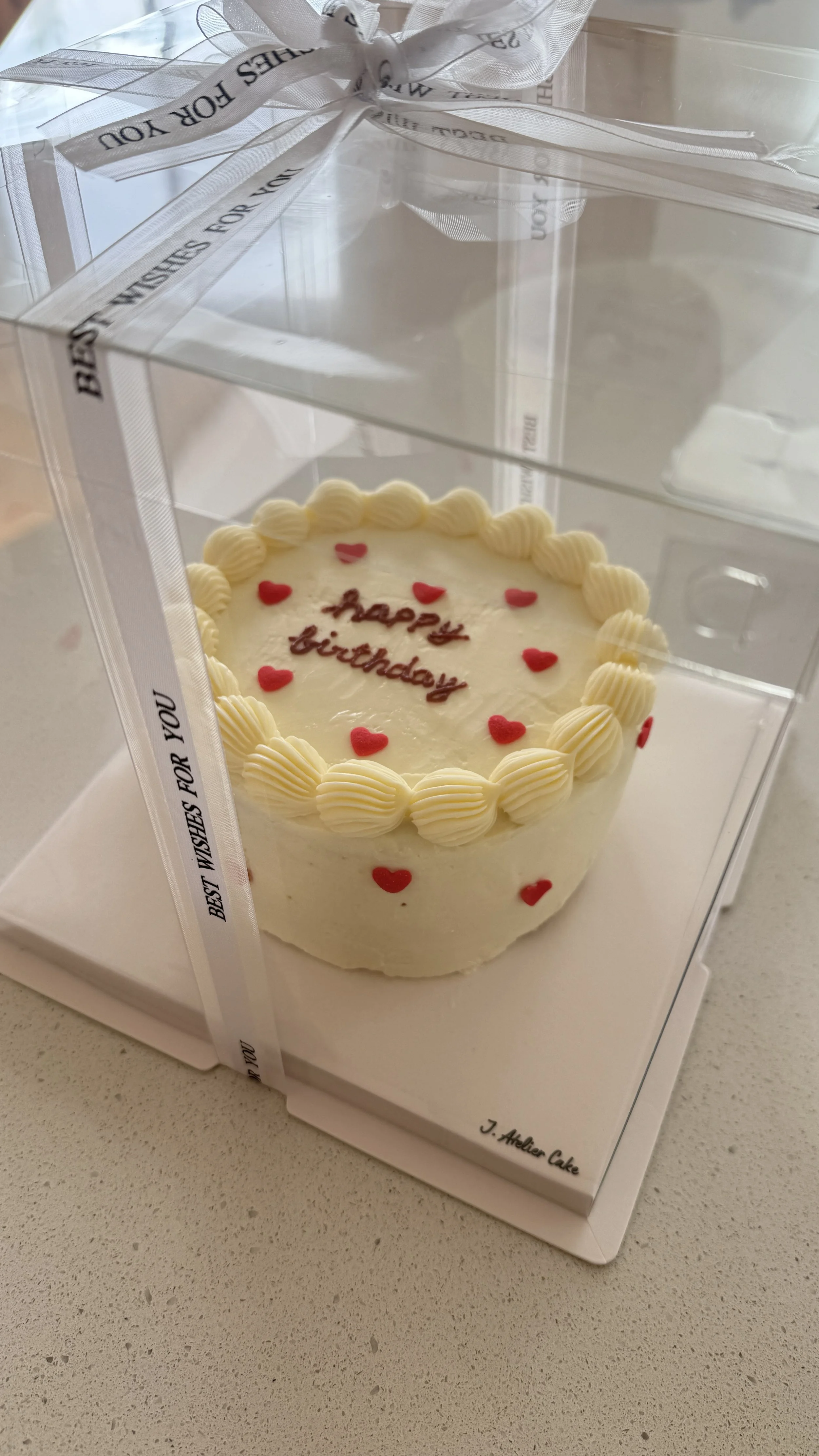 Minimalist Korean-style birthday cake with vintage cream piping, red heart details, and “Happy Birthday” lettering, presented in an elegant clear gift box.