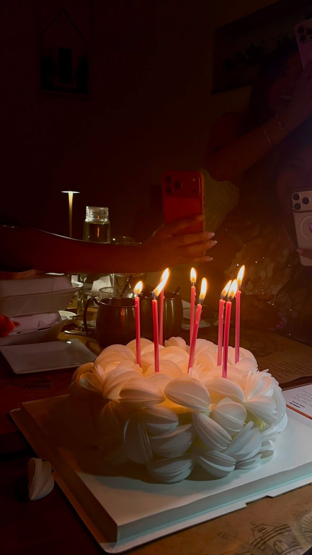 Elegant white Korean-style birthday cake with delicate petal piping and pink candles, photographed during a warm candlelit birthday celebration.
