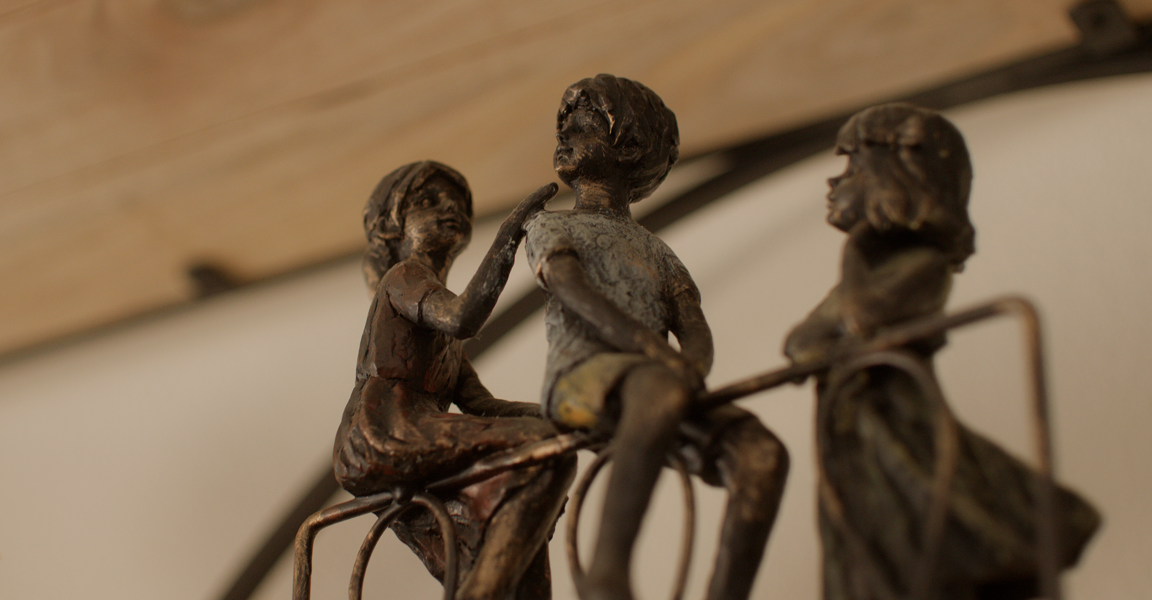 Close-up of three small metal sculptures of children sitting and talking, mounted on a wall.