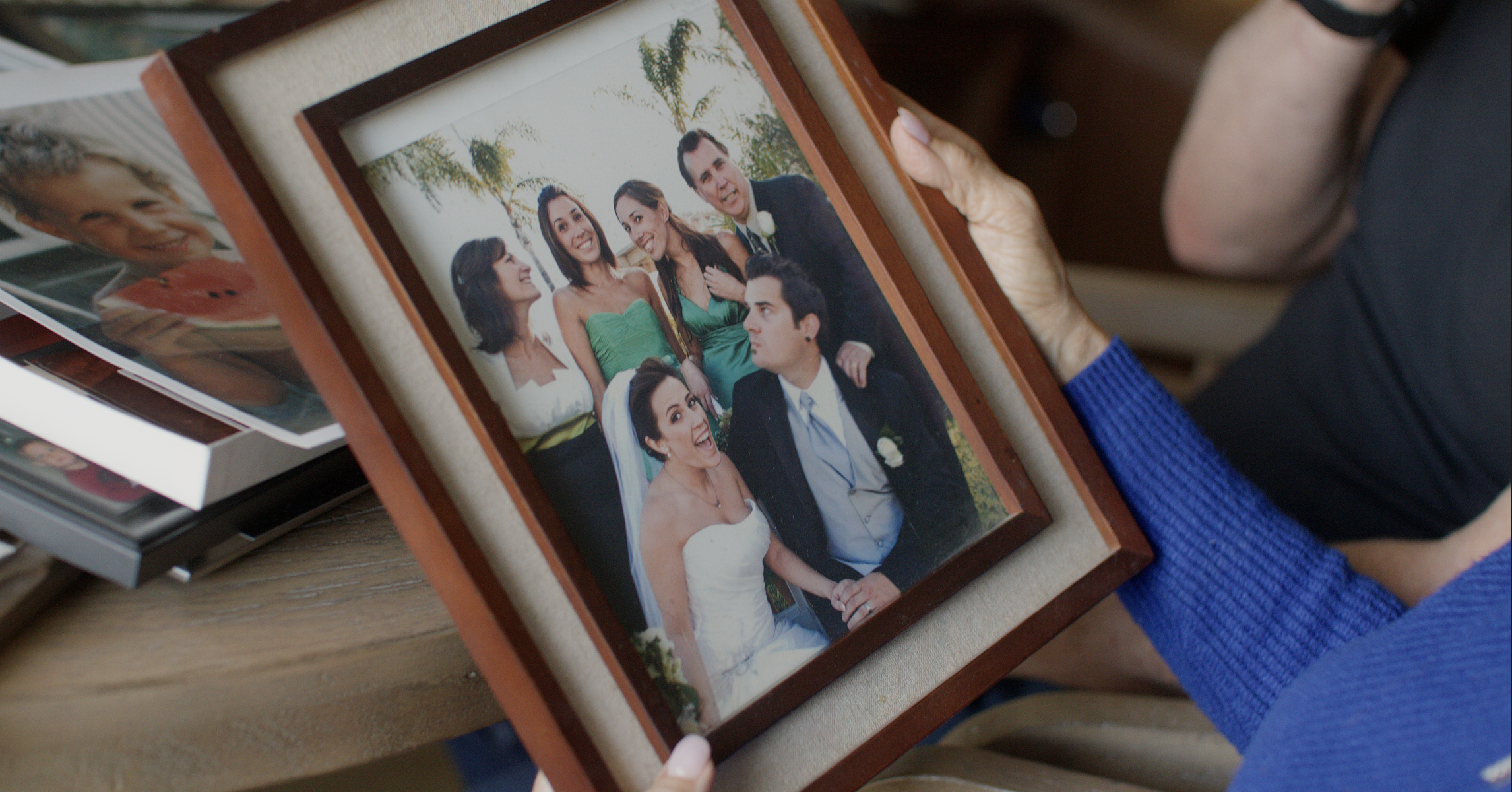 Person holding a framed photo of a wedding party, including a bride and groom, with other guests smiling around them.