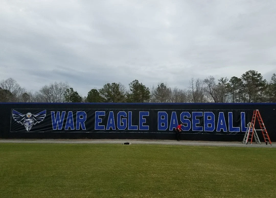 Large Sports banner with the words "WAR EAGLE BASEBALL" and an eagle logo, on a baseball field in a cloudy outdoor setting by Custom Graphics Georgia North Metro Atlanta Sign Installation and Service