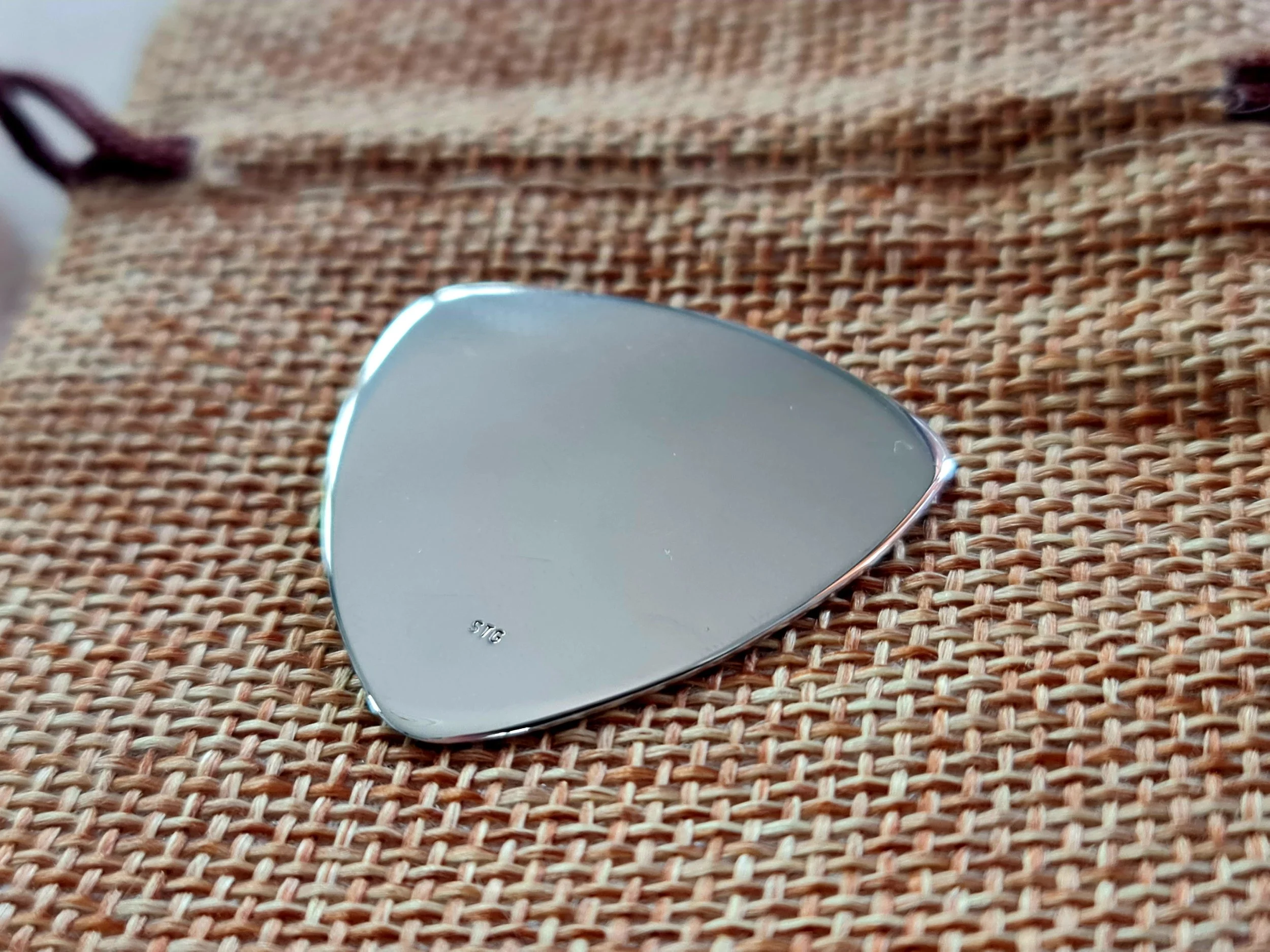 Close-up of a shiny, high polish Carson Sterling silver pick in a triangle shape on a woven canvas pouch.