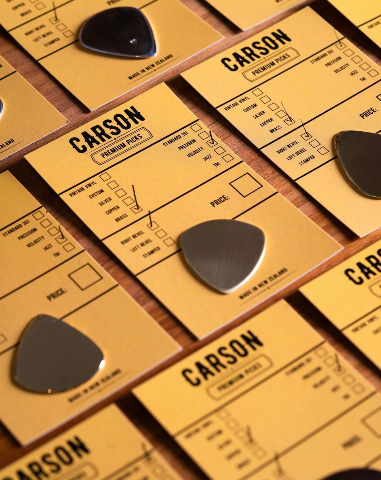 Multiple yellow guitar pick ordering slips with checkboxes for different options, accompanied by guitar picks, on a wooden surface. Text saying "Carson Picks"