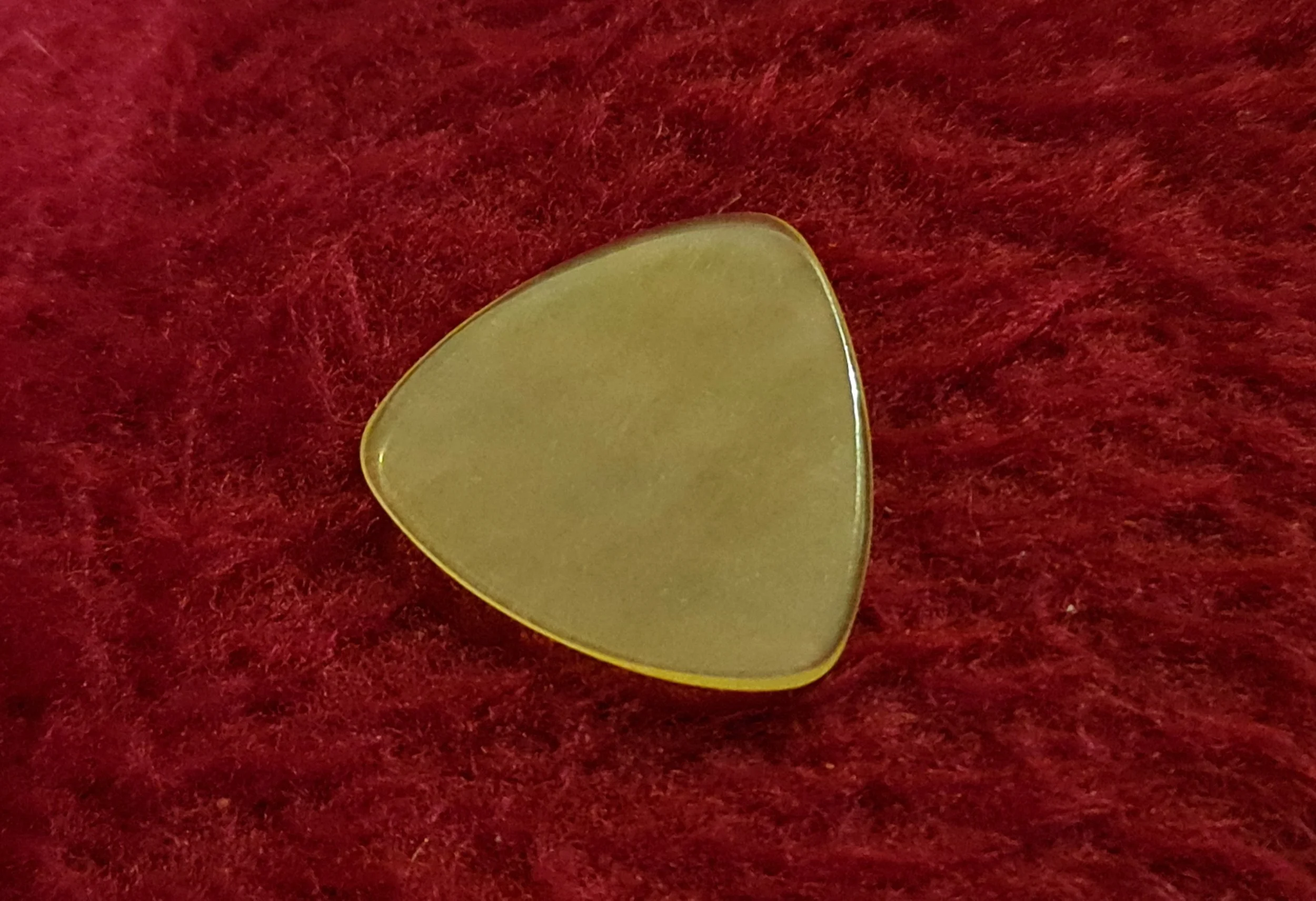 A yellow tortoiseshell guitar pick custom made by Carson Picks resting on a red fuzzy surface.