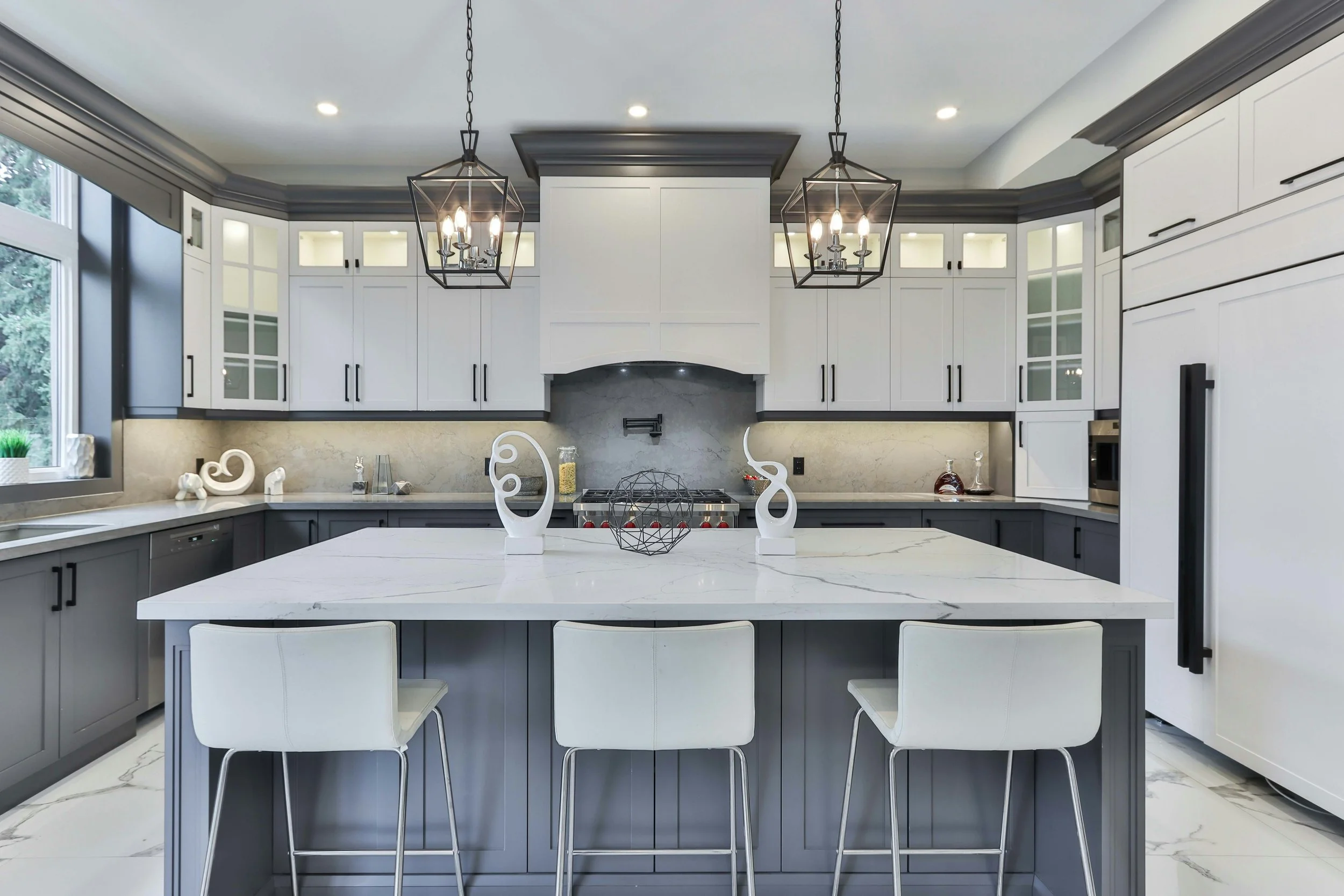 Modern kitchen with white and gray cabinetry, a marble island, and black pendant lights.