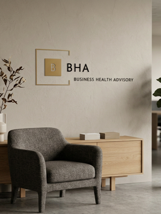 Interior of an office with a gray armchair, a wooden sideboard, and a wall sign that says 'BHA Business Health Advisory'.