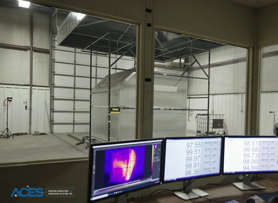 Fire containment test enclosure inside the ACES laboratory, viewed from an observation room with thermal imaging and temperature monitoring screens.