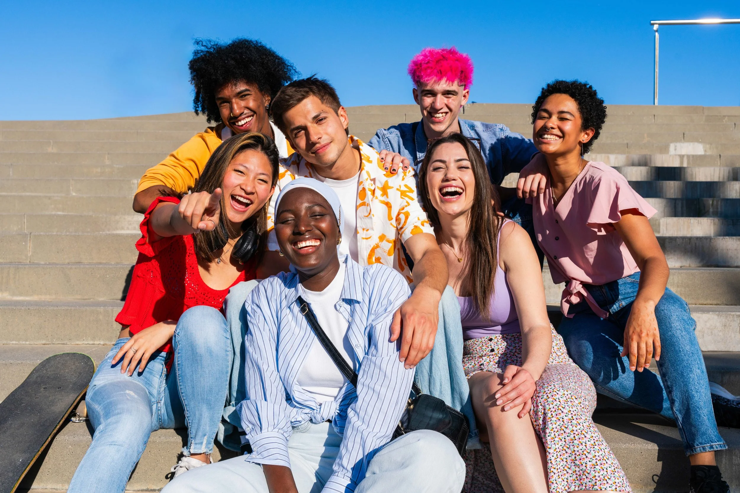 A diverse group of seven young athletes or professionals sitting on outdoor steps, smiling and enjoying a life after sport.