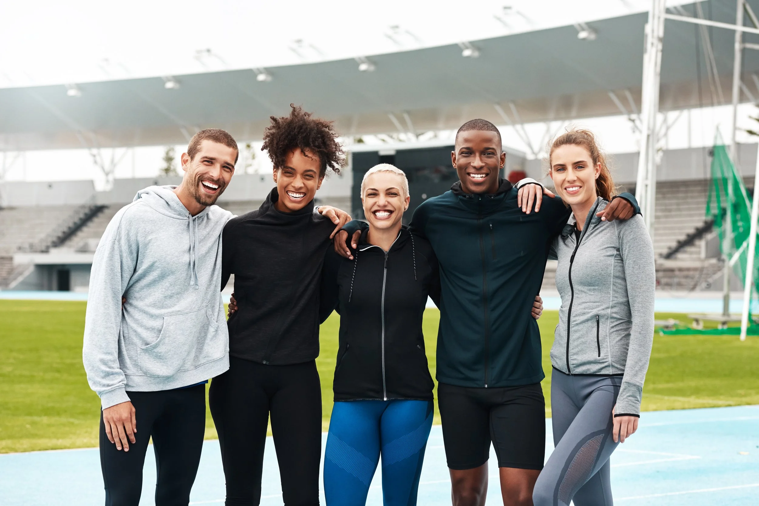 Group of five diverse Elite athletes smiling and standing together as a team, in a outdoor sports stadium.