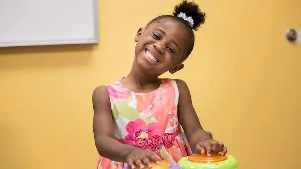 Young girl smiling and playing with a colorful toy in a room with yellow walls.