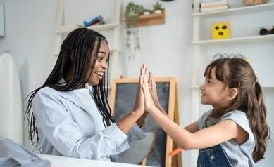A woman and a young girl high-fiving each other in a bright, modern room.