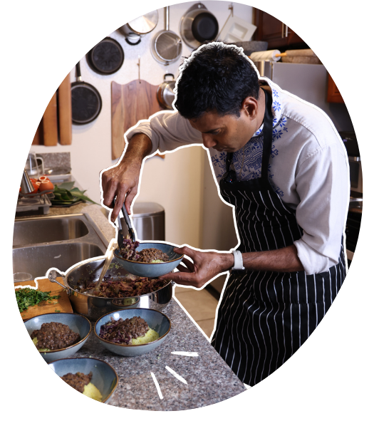 Chef serving cooked food into bowls in a kitchen.