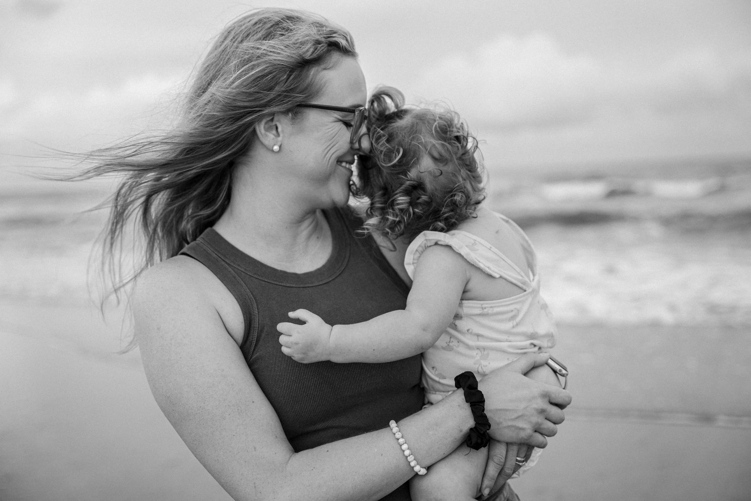 Black and white portrait of a mother holding her child on the beach.