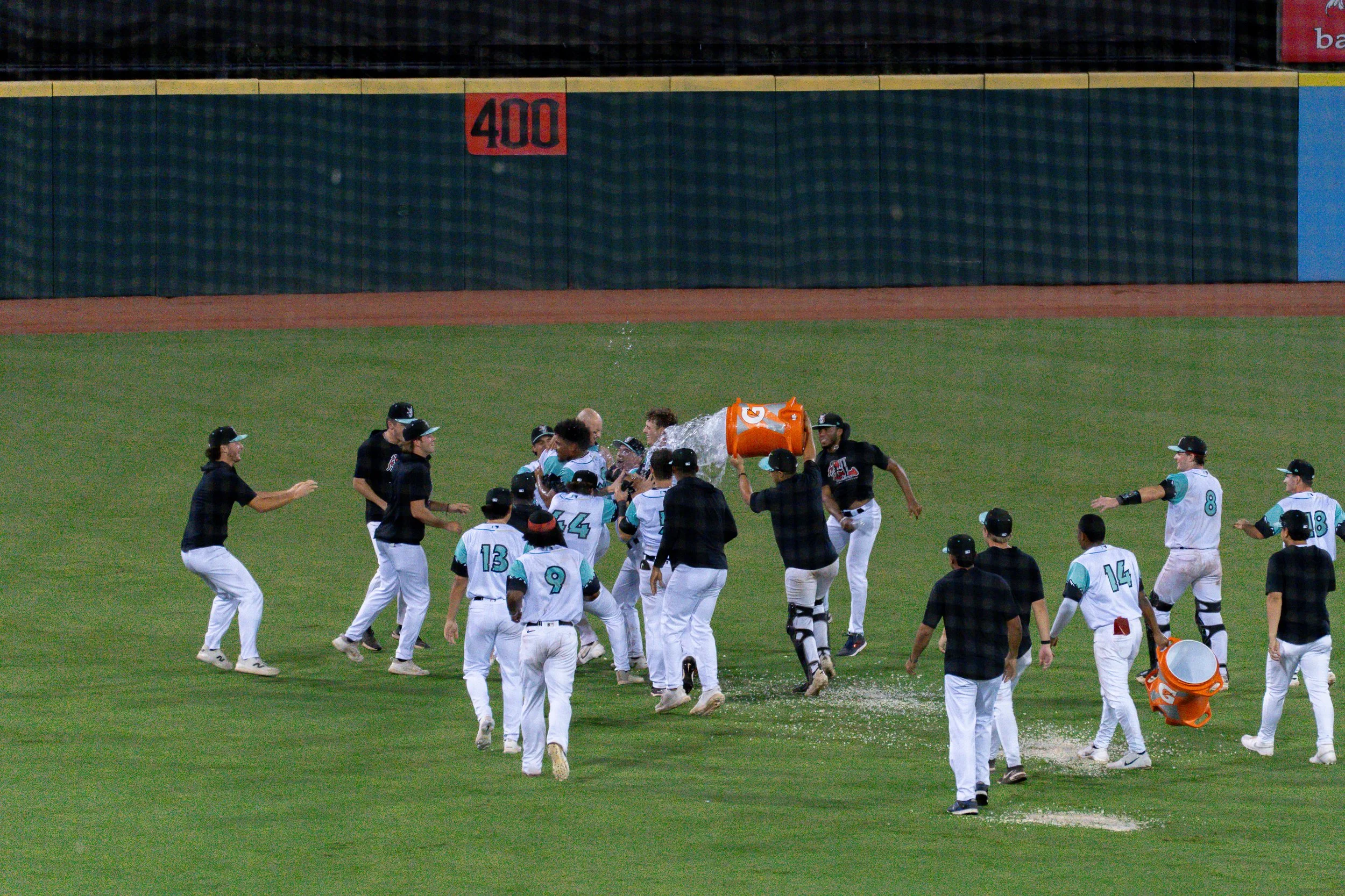 Baseball players celebrating on the field, with one player pouring water from a bucket over another player.