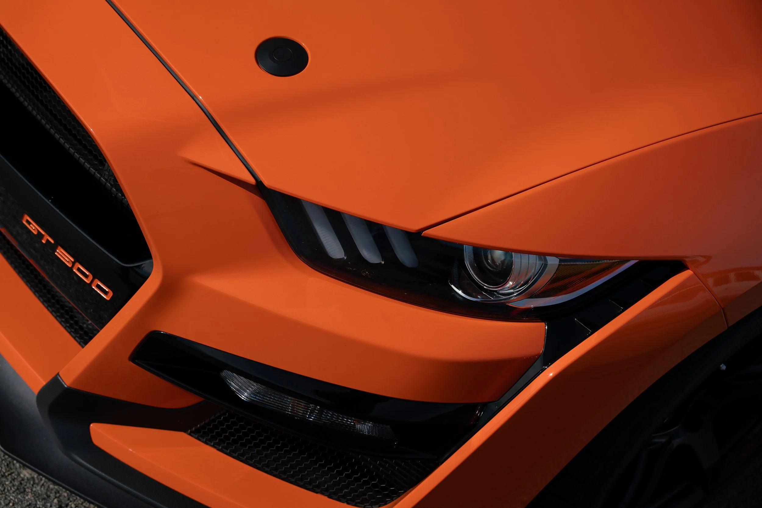 Detail photograph of an orange Mustang GT350 featuring the headlight and front grill. 
