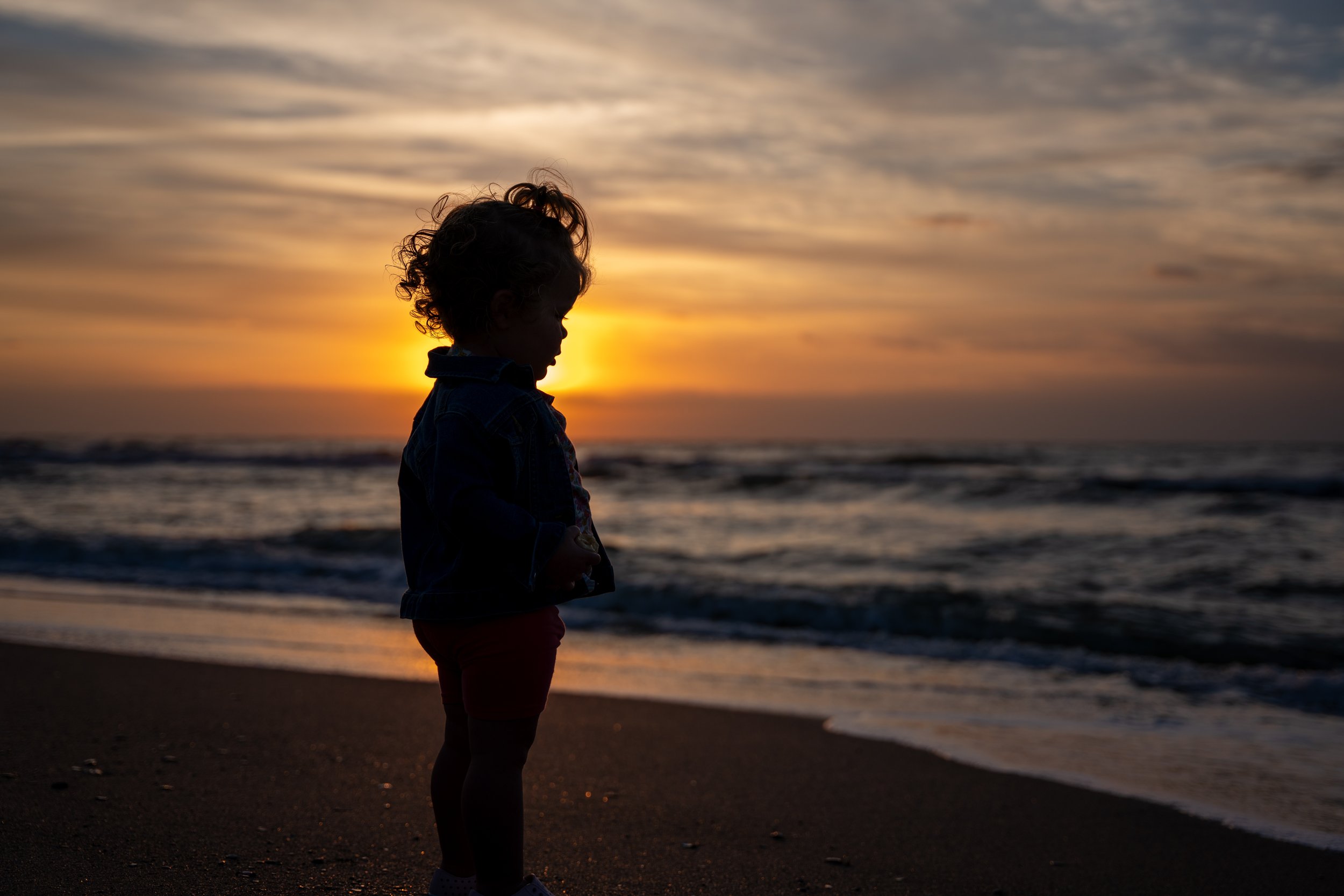 Silhouette portrait of a young girl on the beach at sunset with the ocean and colorful sky in the background. 
