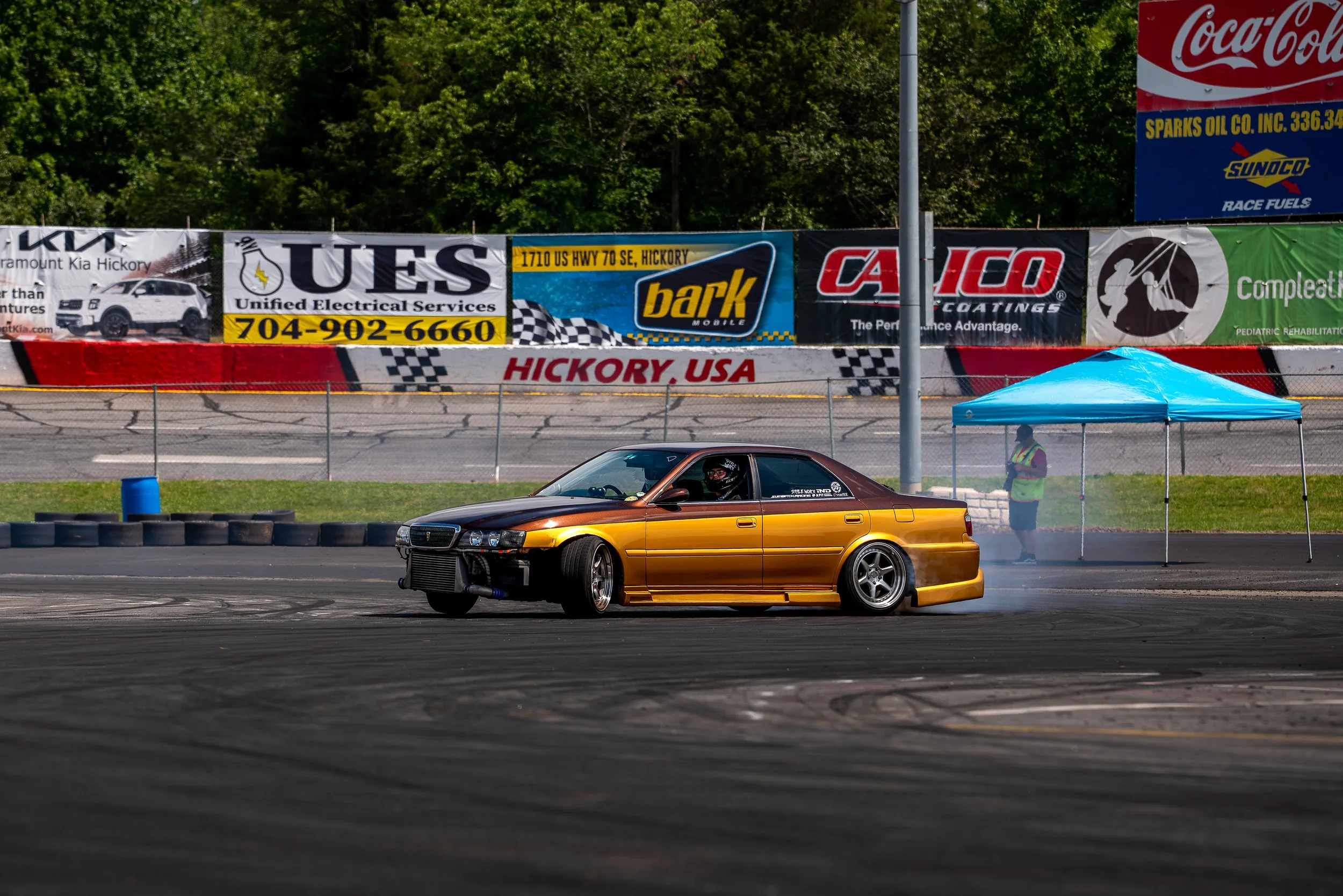 Gold and black drift car producing smoke during a drift event.