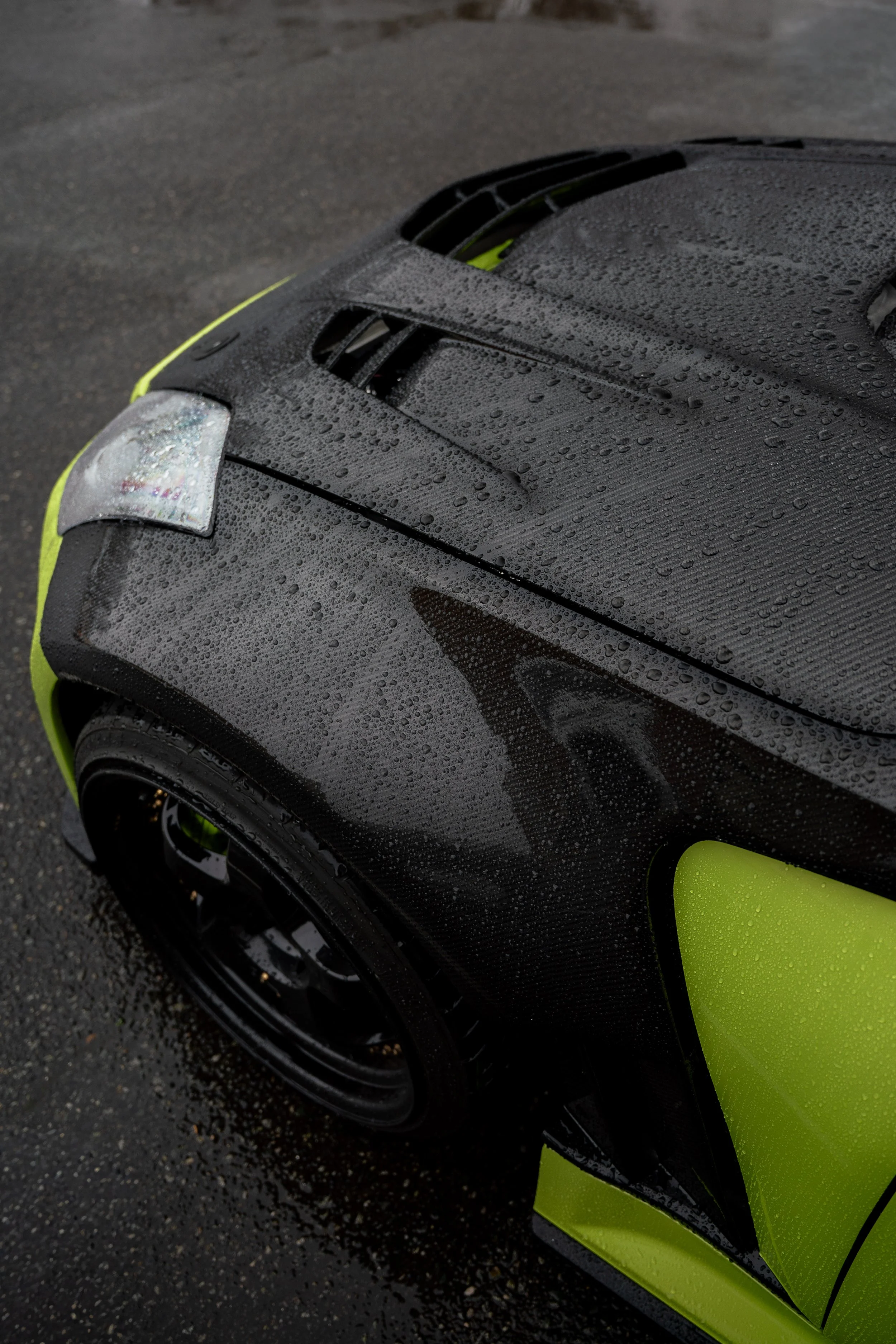 Close-up automotive photography of a black sports car with neon yellow accents in the rain.