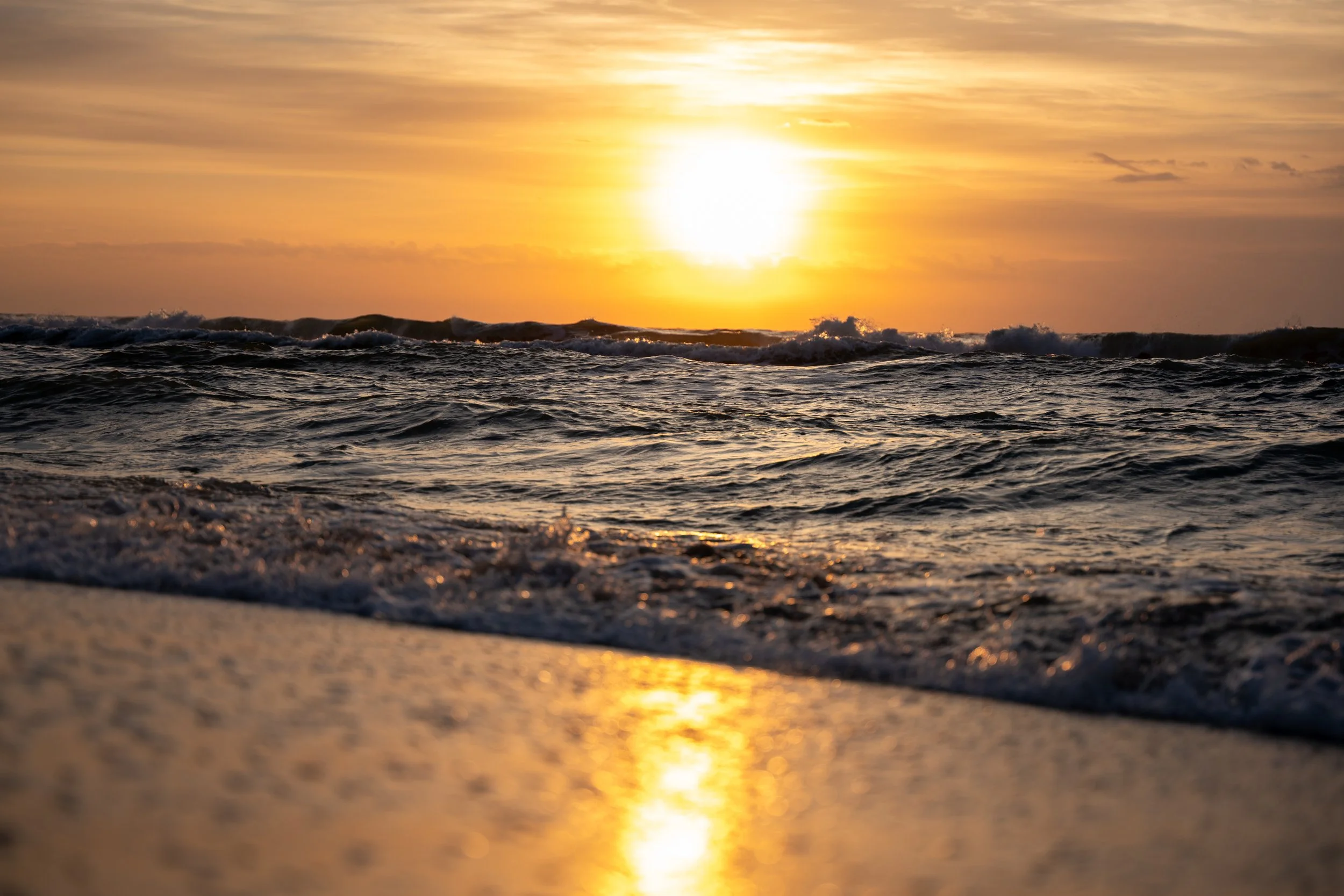 Golden sunset over the ocean with waves reflecting across the shoreline.