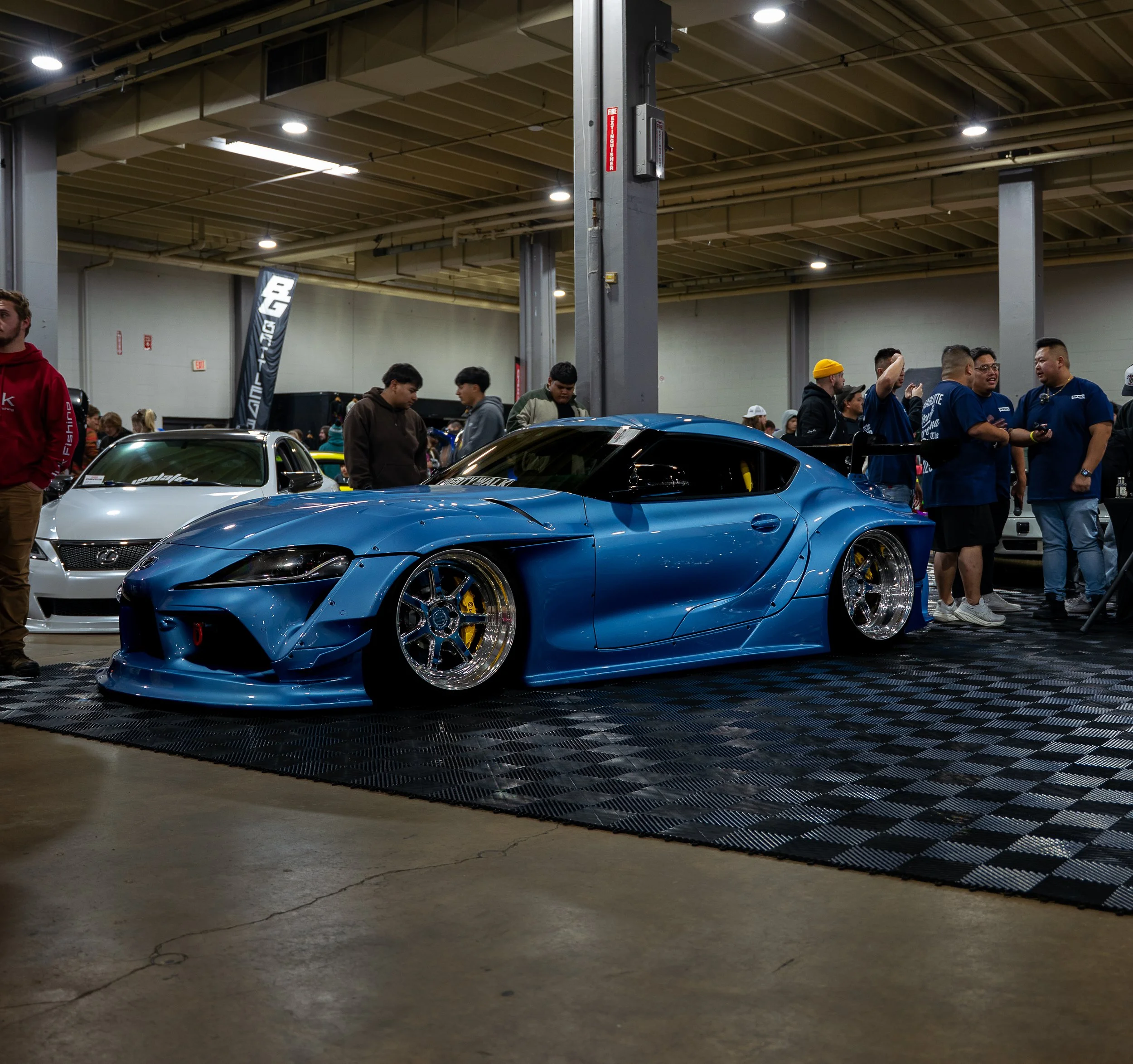Blue Supra on display at an indoor automotive event with attendees exploring the show. 
