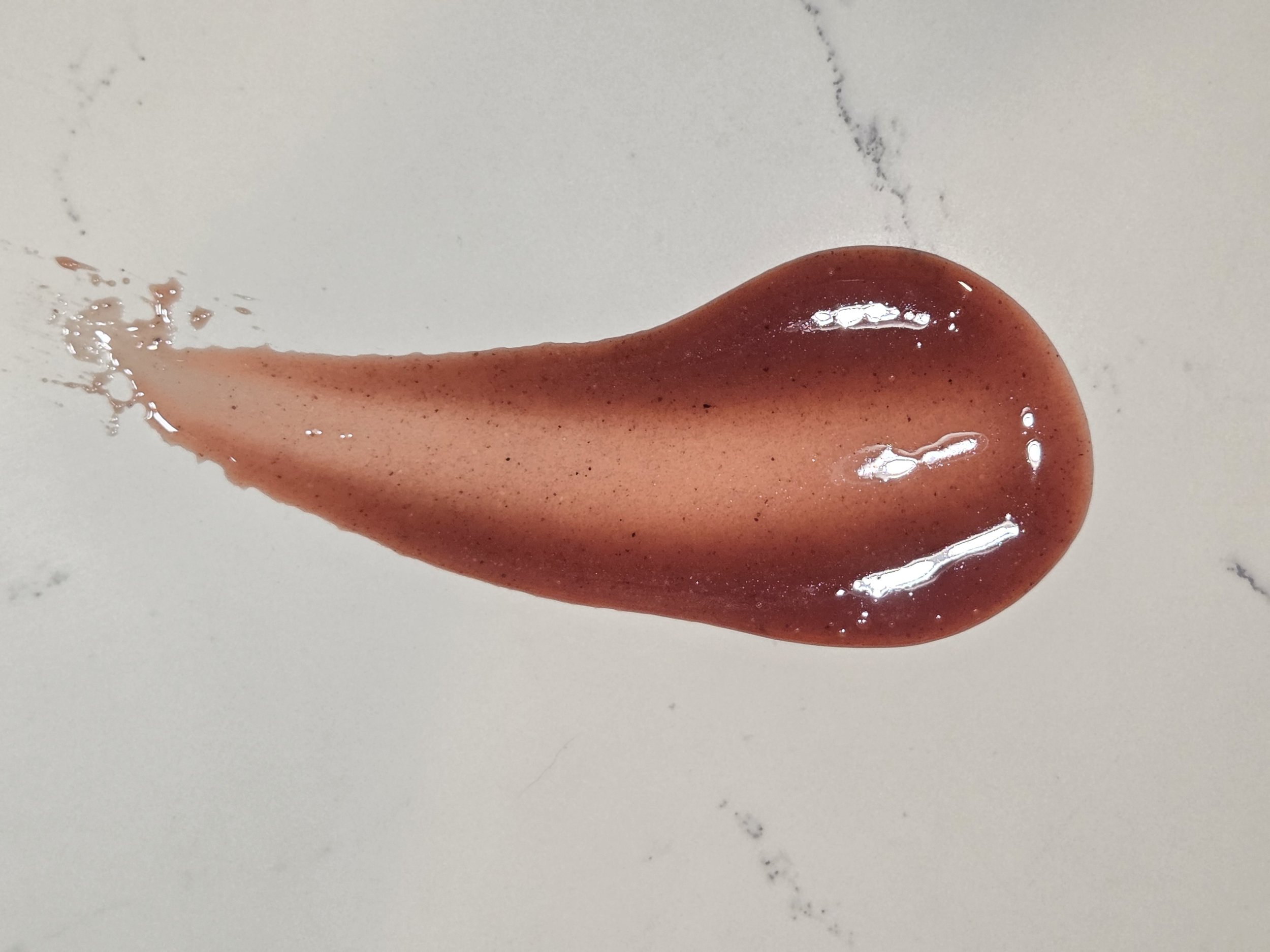 A smear of reddish-brown ketchup on a white surface with some splatters around it.