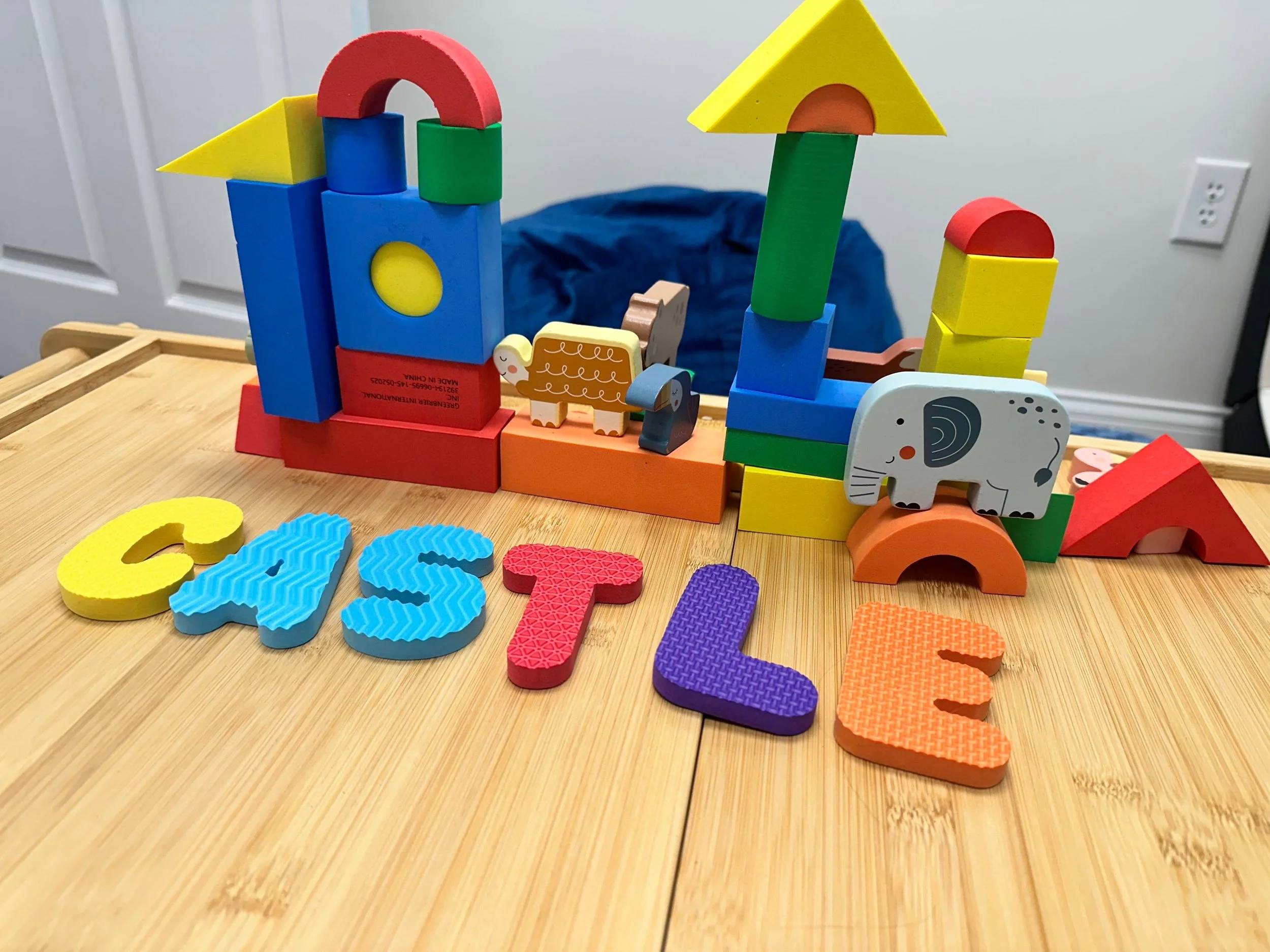 Colorful children's building blocks arranged to resemble a cityscape with letters spelling 'CELE' and animal figures, sitting on a wooden surface.