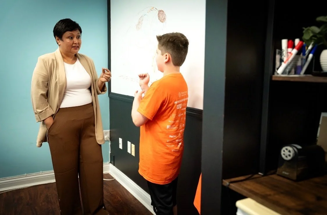 A teacher standing and talking to a boy in a classroom near a whiteboard.