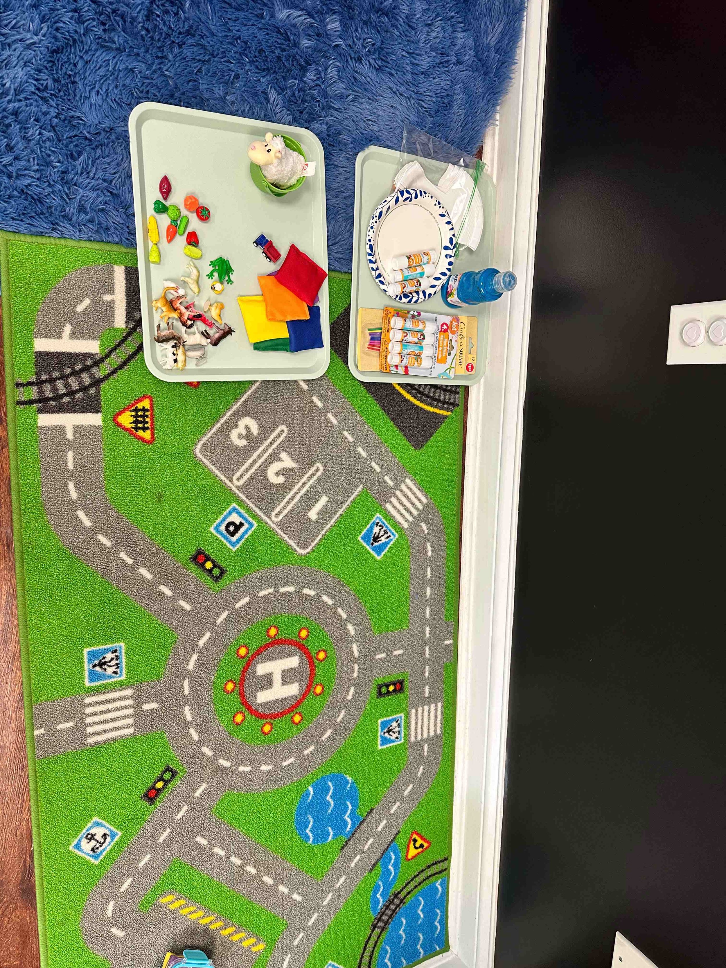 Colorful educational play mat with a road map design, featuring various traffic signs, water bodies, and a helipad, with toys placed on top.