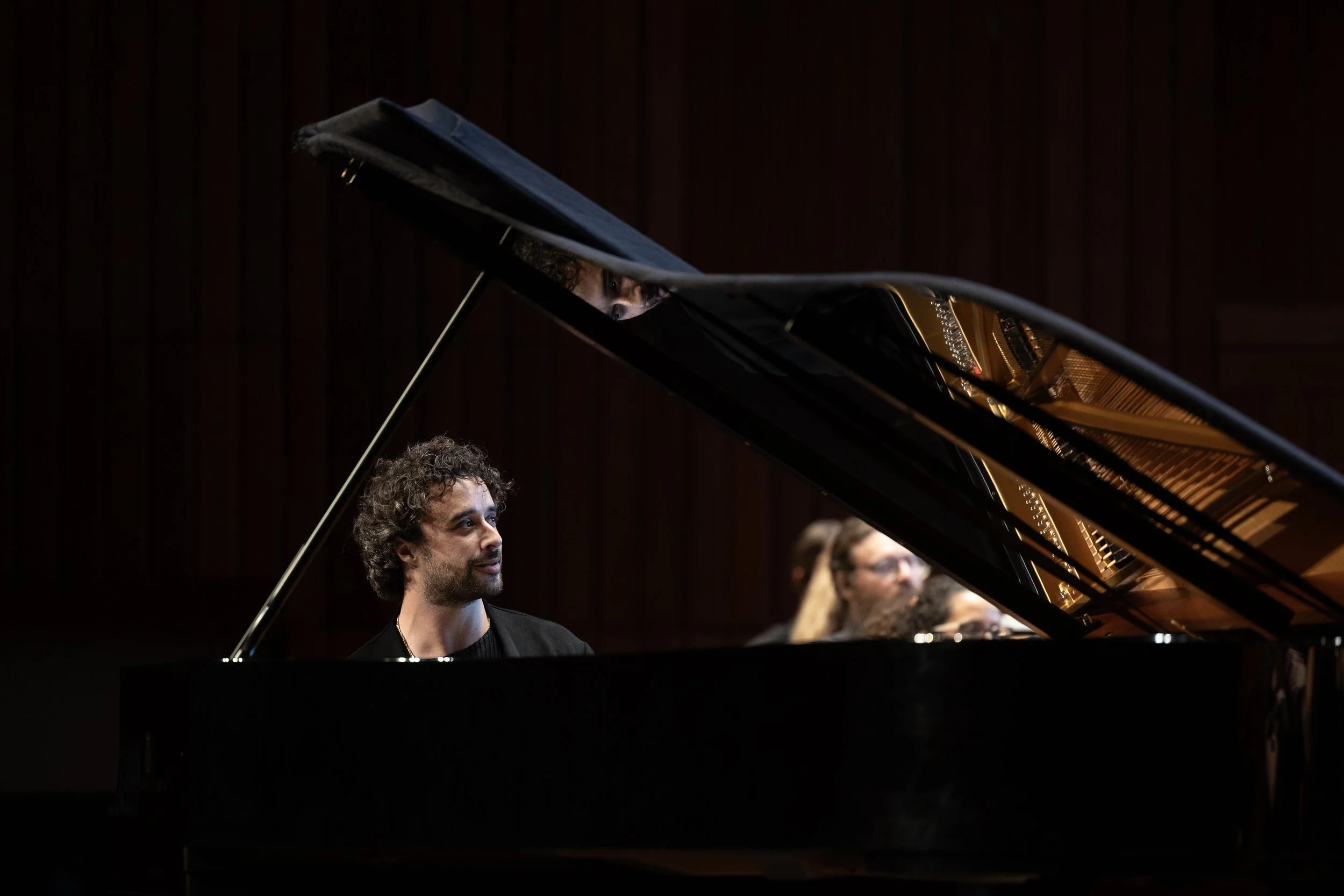 Raúl da Costa sitting at a grand piano, with an expression of concentration, as part of an orchestra during a performance.