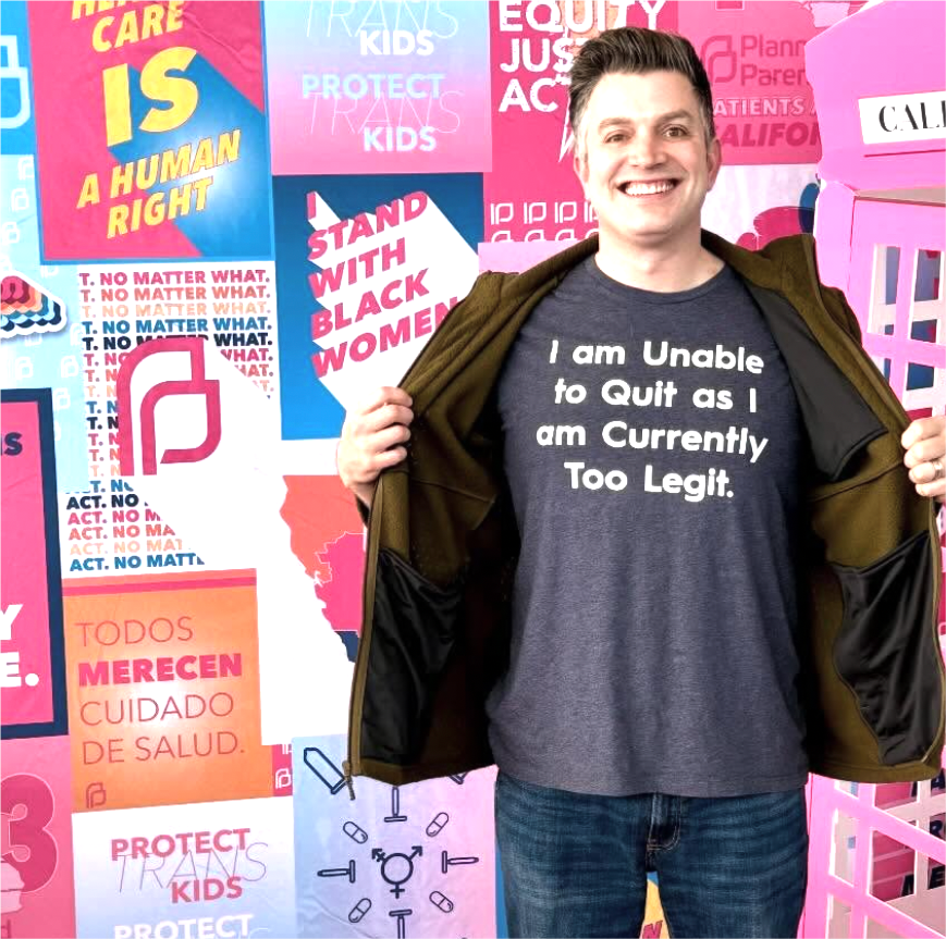 Man smiling and opening his jacket to reveal a t-shirt that reads 'I am Unable to Quit as I am Currently Too Legit'.