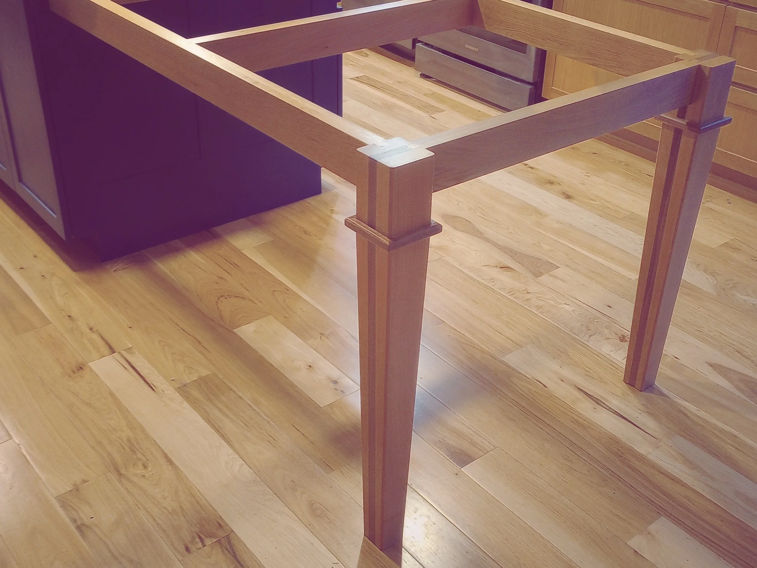 Unassembled wooden kitchen cabinet frame on a hardwood floor.