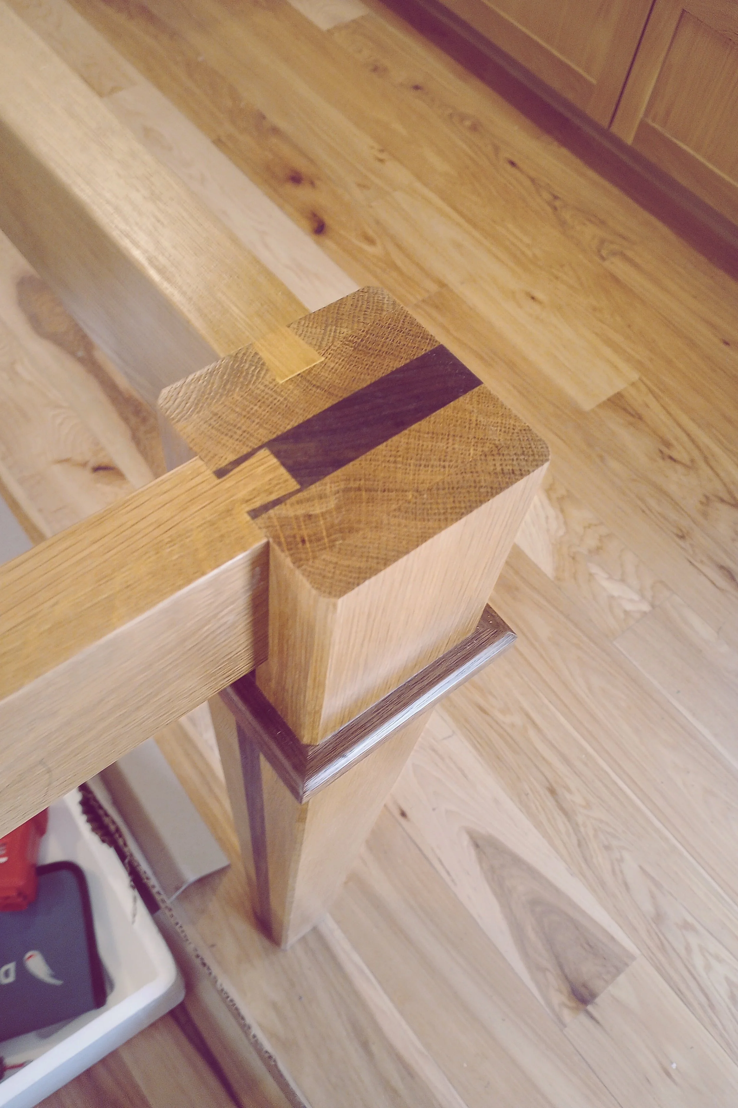 Close-up of a wooden post with a dark stain on the top corners, part of a wooden railing or structure, and a wooden floor in the background.