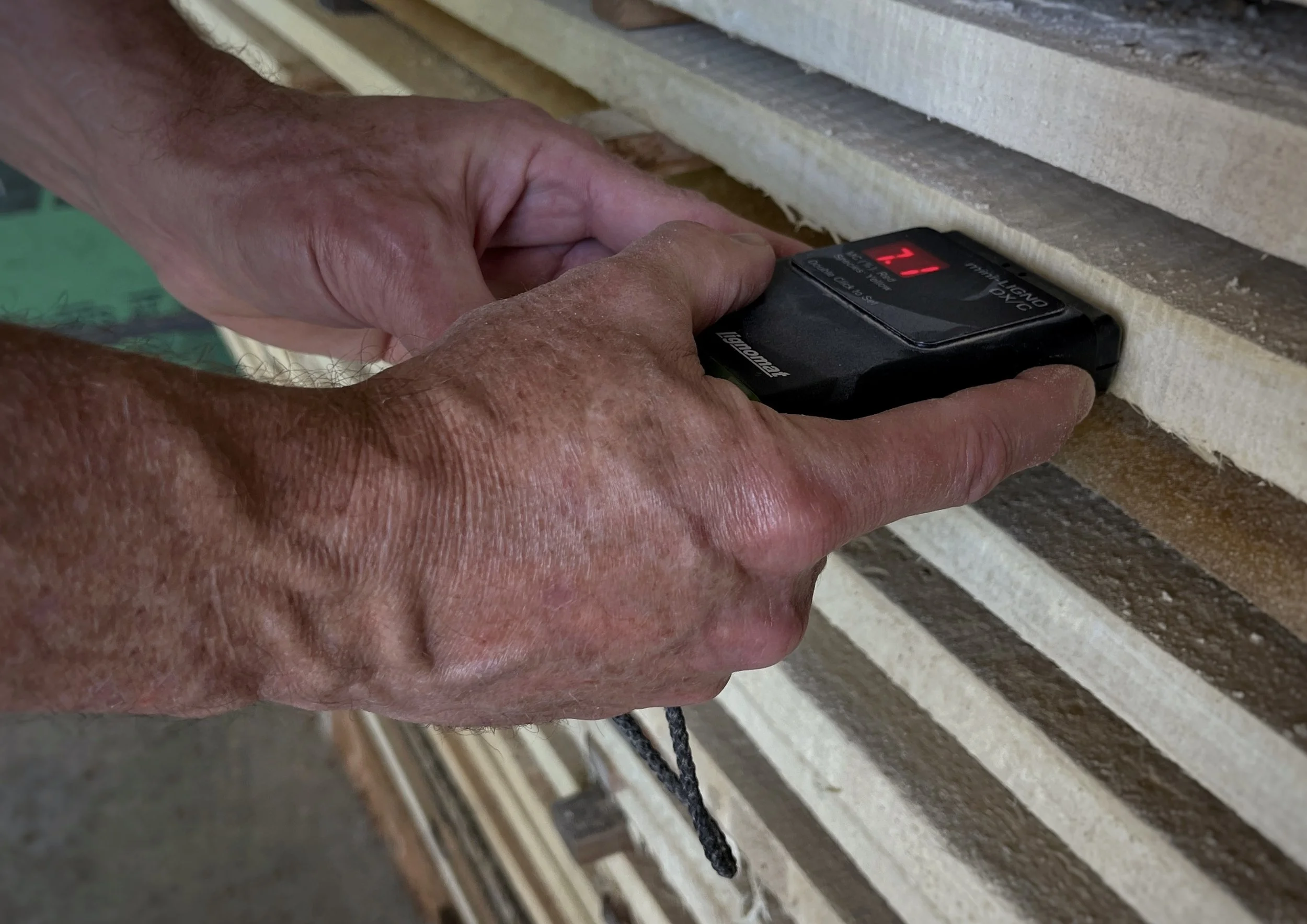 A person's hands holding a laser temperature scanner measuring the temperature of wooden planks.