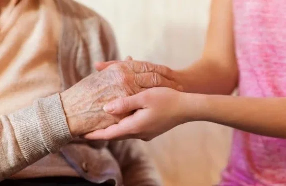 Two people holding hands, one elderly and one younger, in a caring gesture.