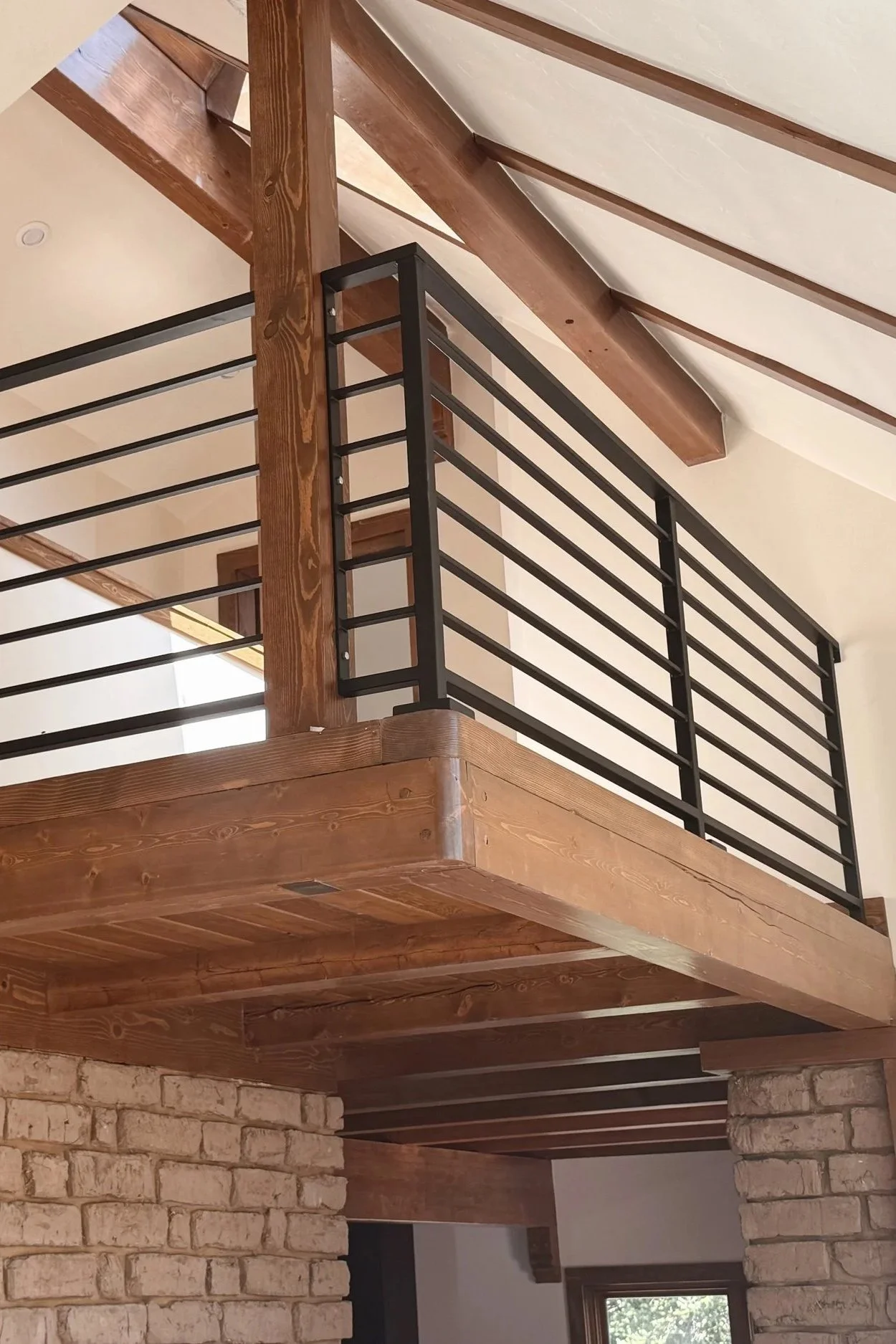 Interior view of a wooden loft with brick columns and a black metal railing, showcasing a modern rustic architectural style.