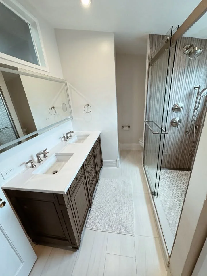 Bathroom with a double sink vanity, large mirror, towel rings, and a separate glass-enclosed shower with multiple shower heads.