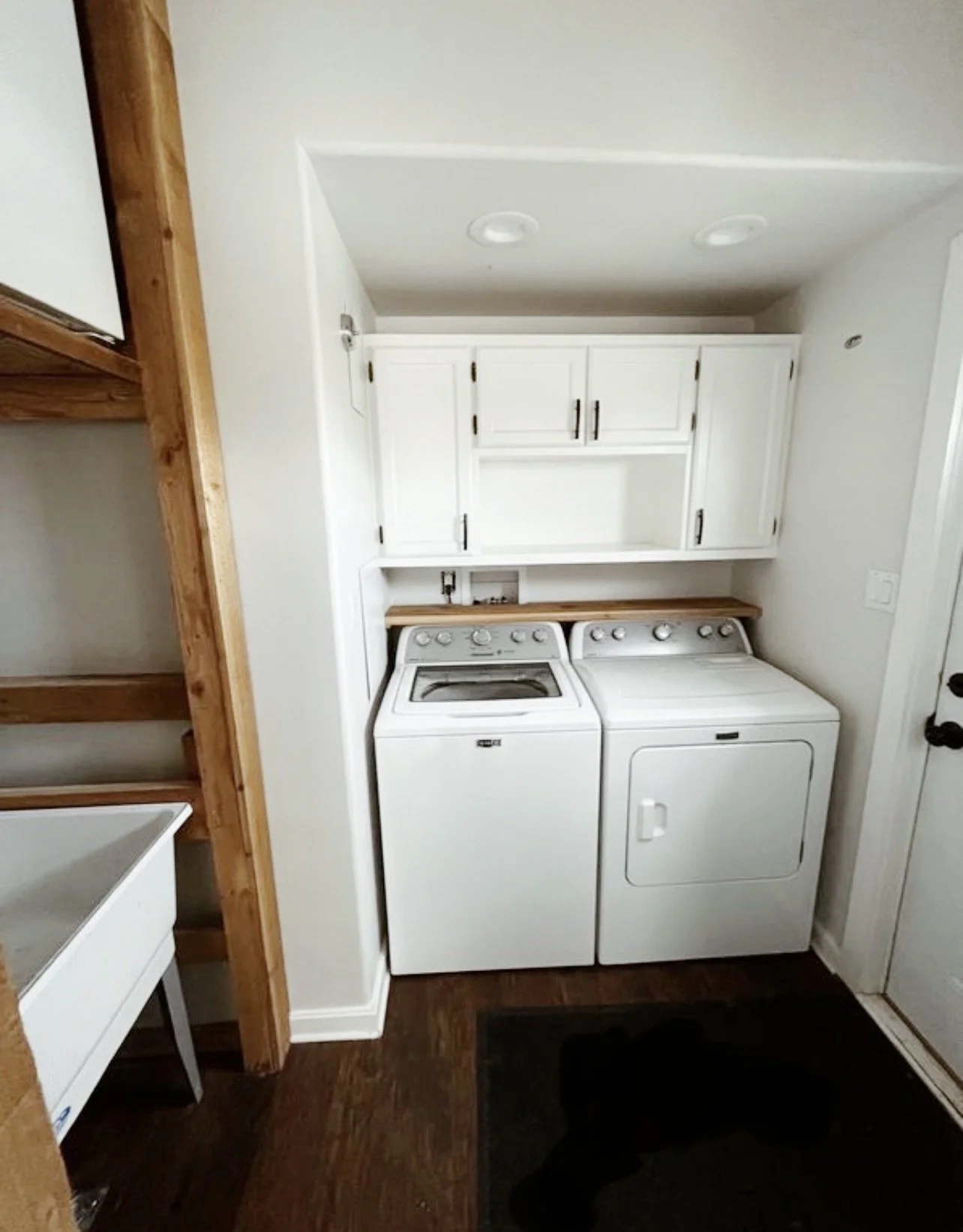 Laundry room with white washer and dryer, white cabinets above, wooden countertop, and dark hardwood floor.