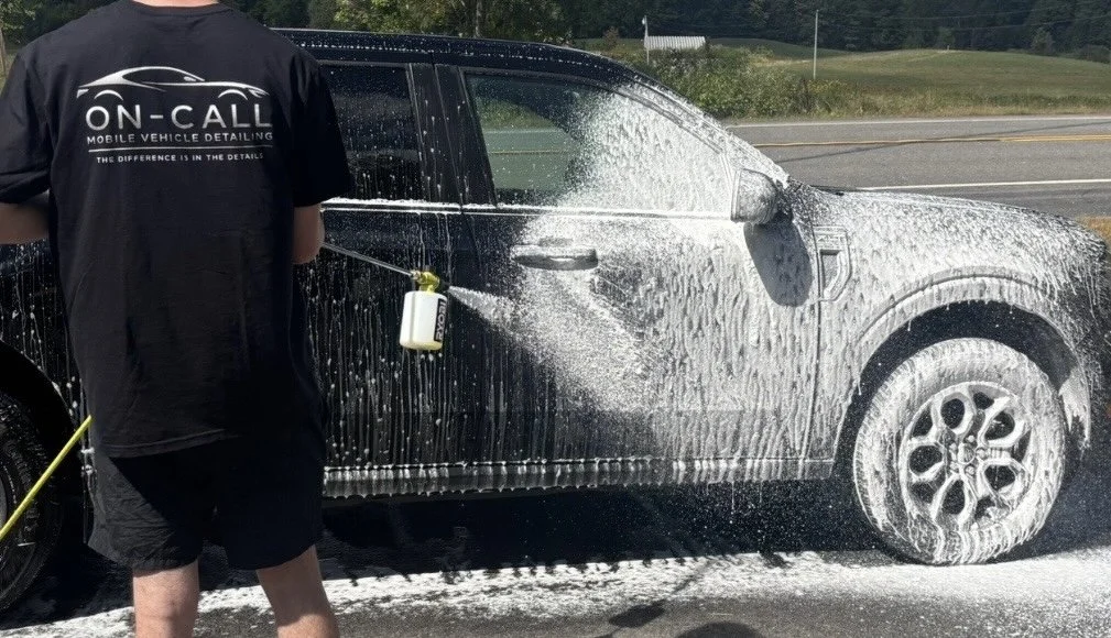 Person washing a black SUV with soap and water on a roadside.