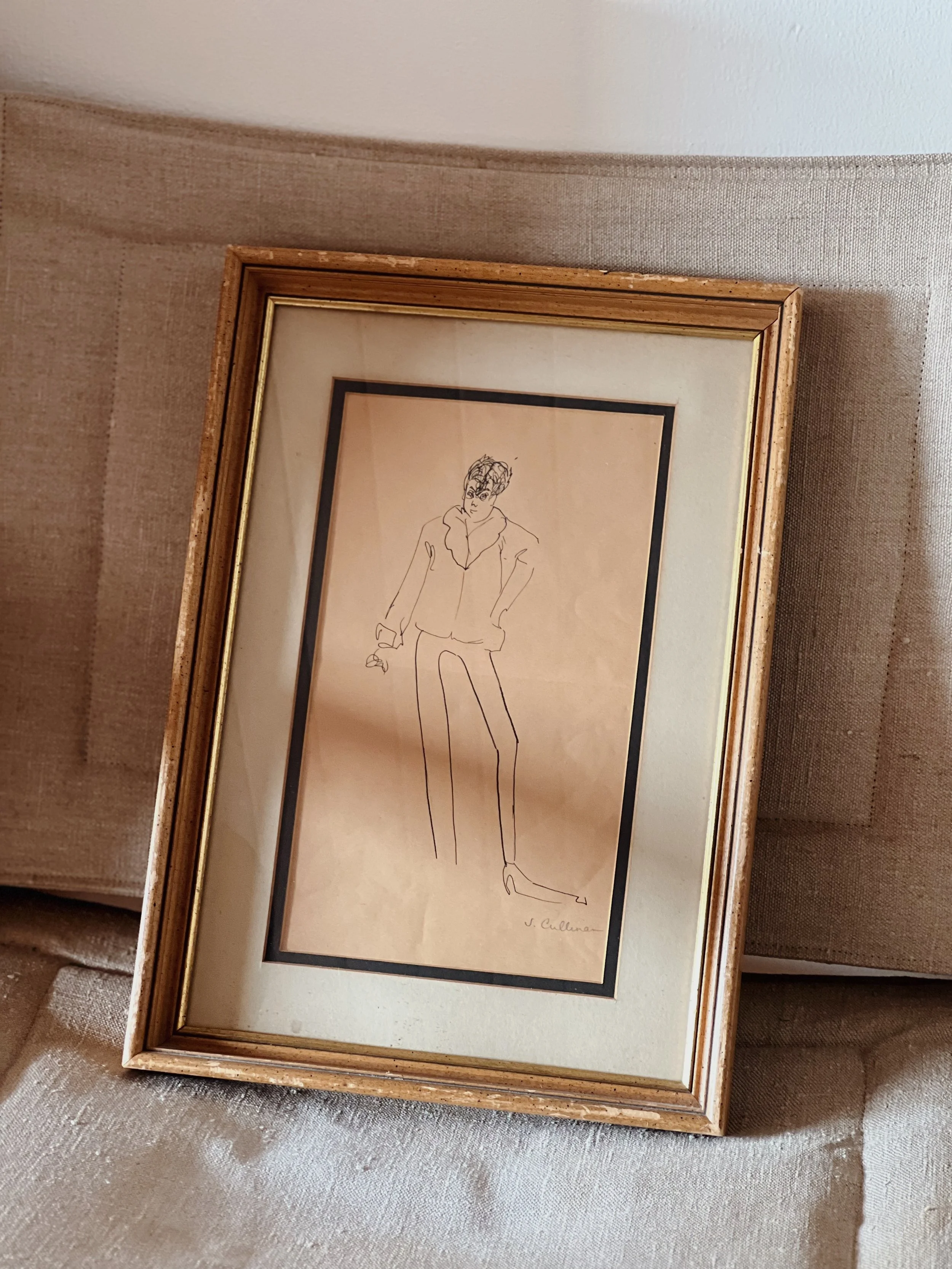 Framed sketch of a person with curly hair, wearing a jacket, with the signature 'J. Cullinan' at the bottom right corner, resting on a beige textured fabric surface.