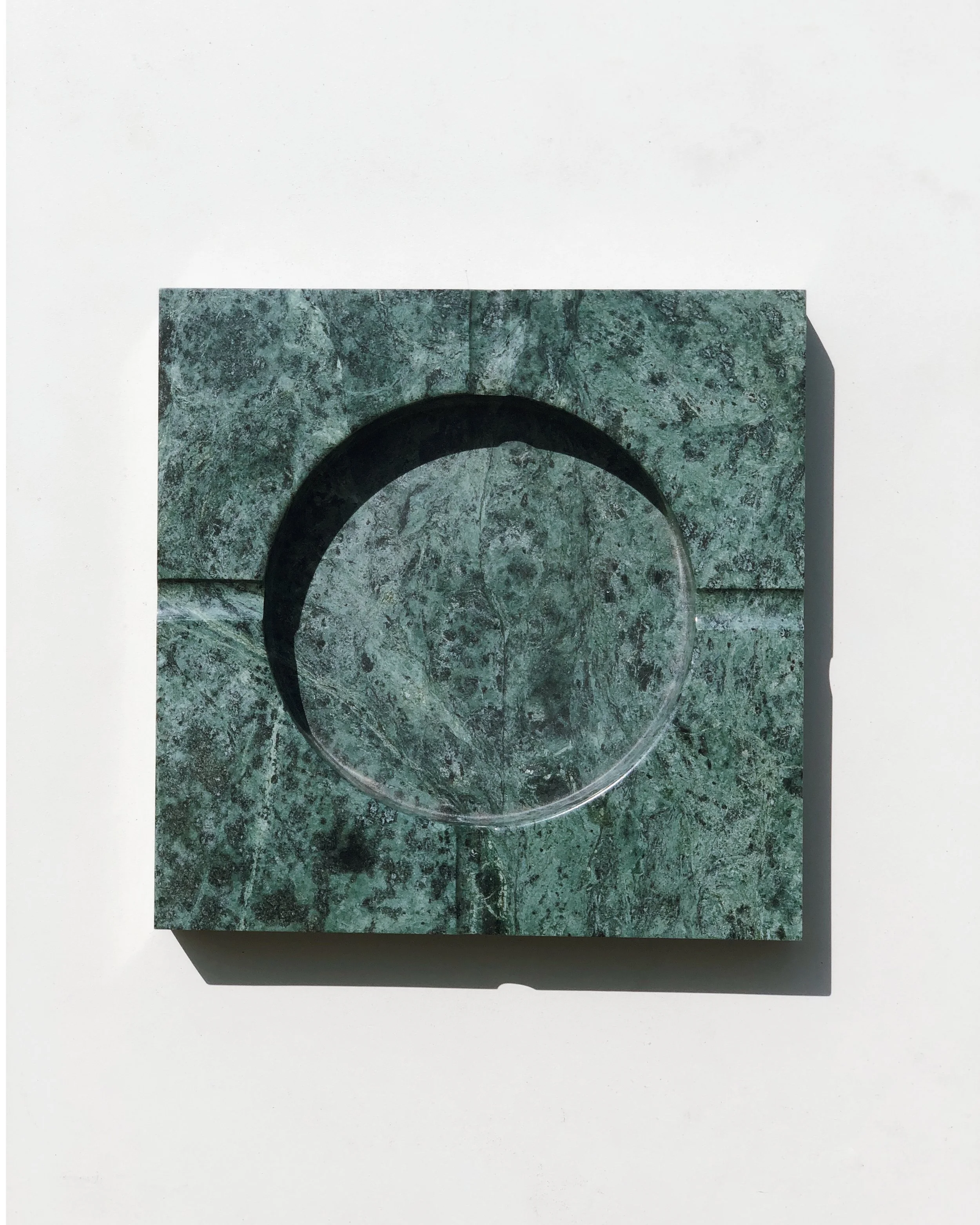 Close-up of a marble or granite square block with a circular cut-out in the center, against a white background.
