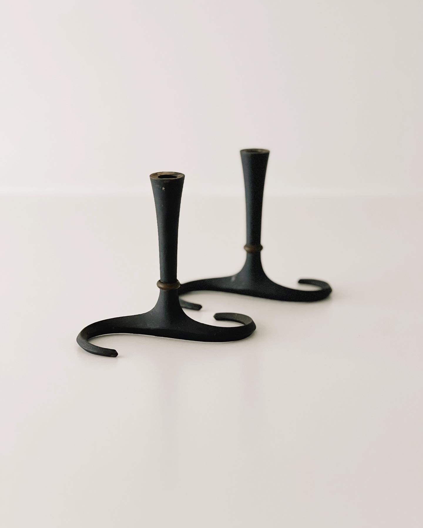 Two vintage black metal candle holders with curled bases and tapered stems on a white surface and background.