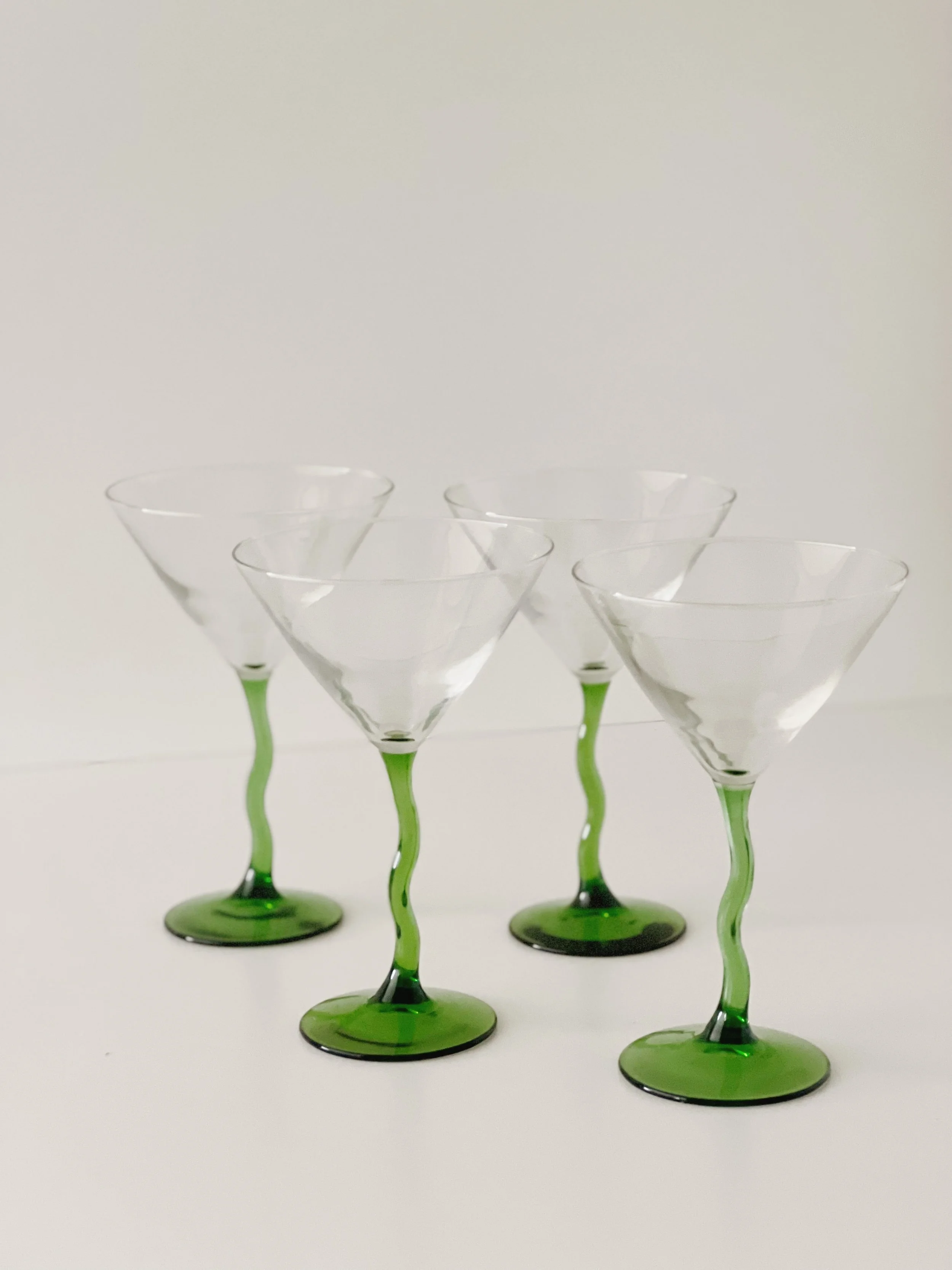Six martini glasses with green stems and bases arranged in a cluster on a white background.