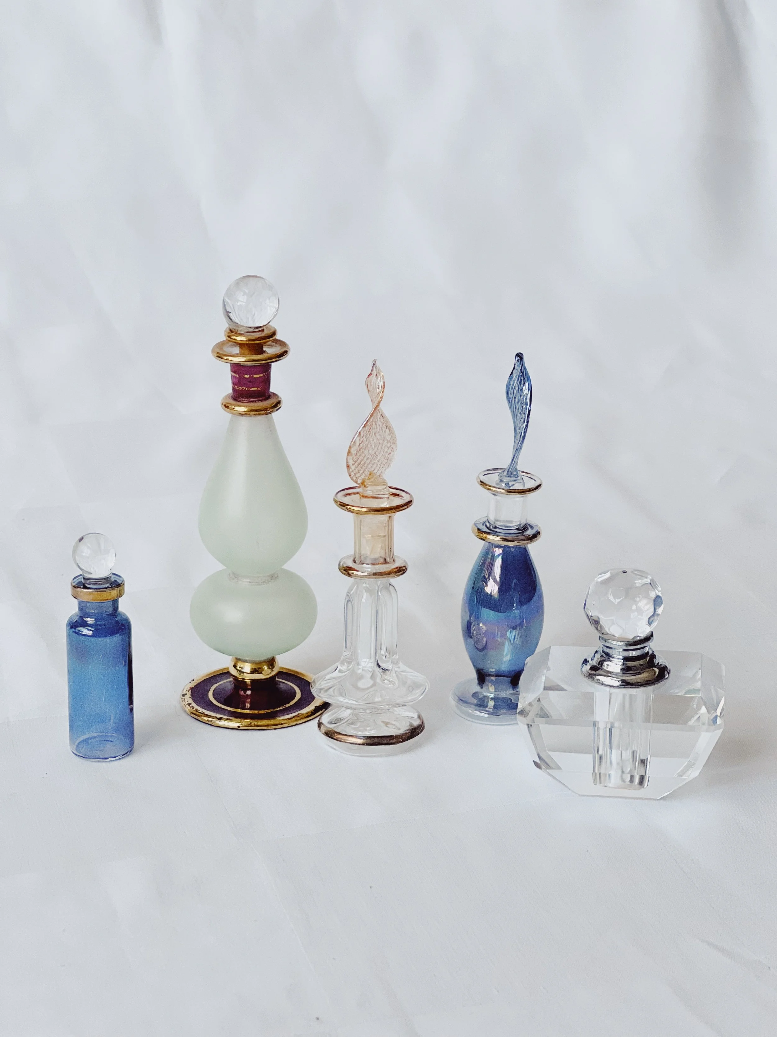 Collection of decorative glass bottles and containers in various shapes, sizes, and colors displayed on a white surface.