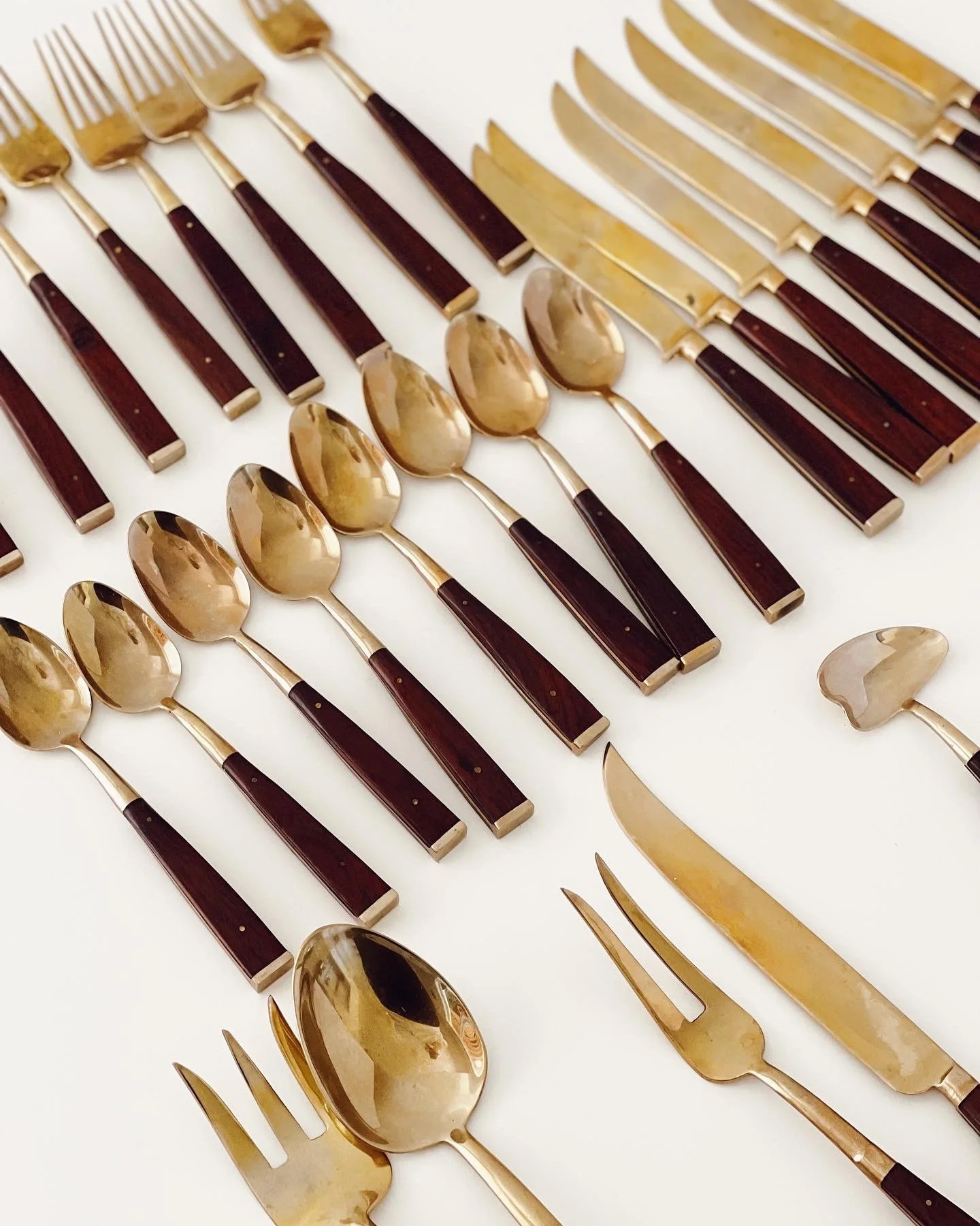 Collection of gold and black cutlery including knives, forks, and spoons arranged on a white background.
