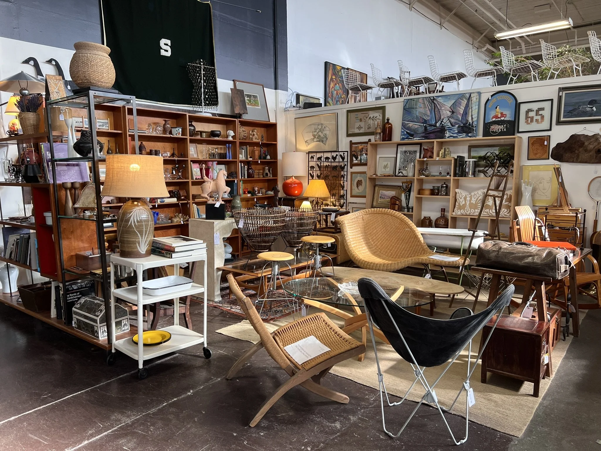Interior of a thrift or antique store with various furniture, artwork, and decorative items displayed on shelves and tables.