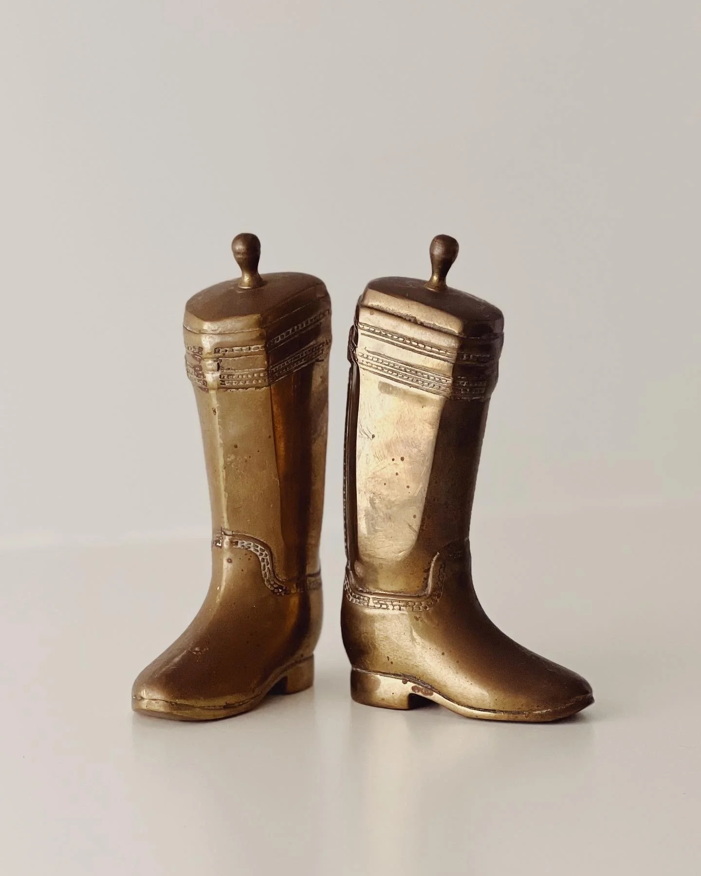Two vintage brass cowboy boot figurines with intricate patterns on the shafts.