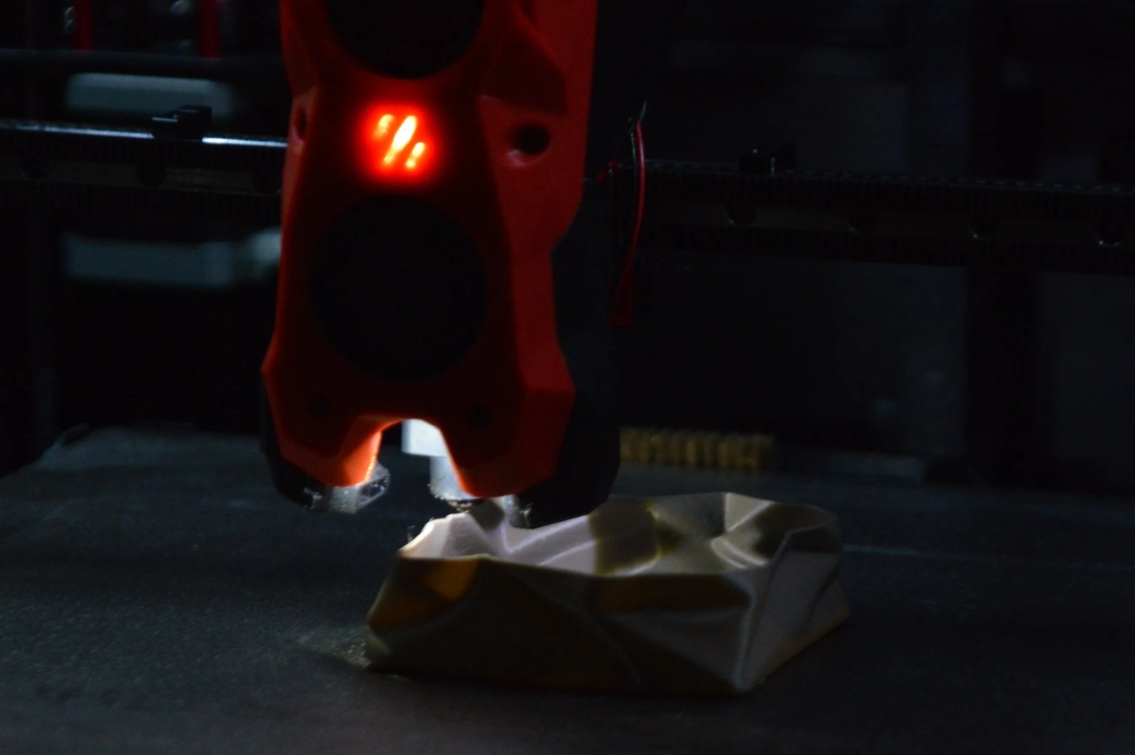 Close-up of a small orange toy dinosaur hanging from a paper bag at a grocery store checkout counter, with other items and a dark background visible.