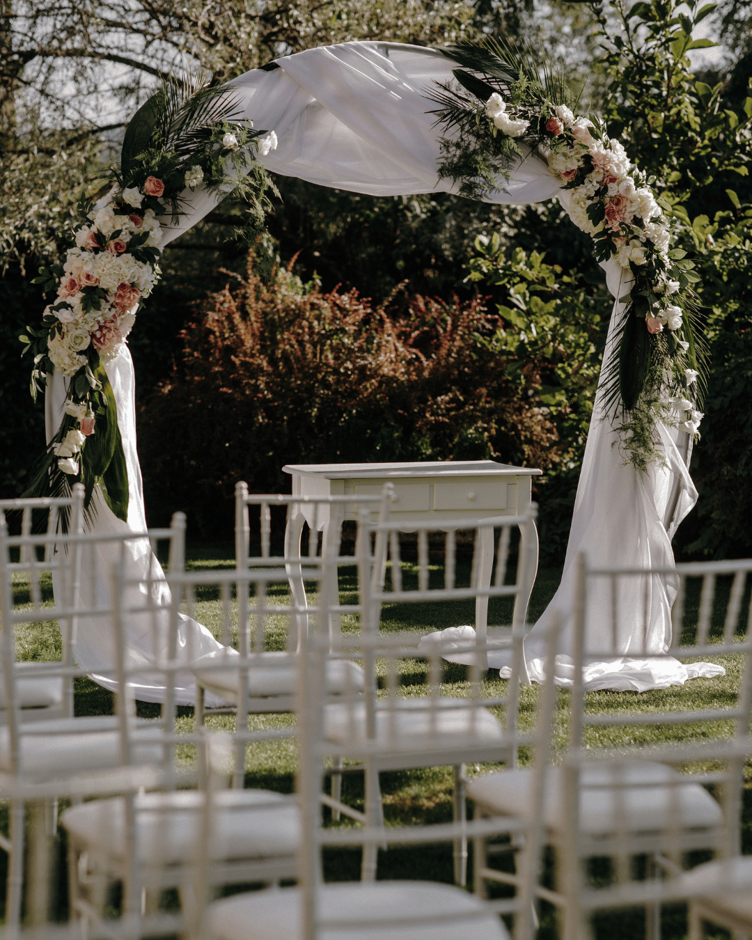 White chiavari chair rentals and a decorated wedding ceremony arbor