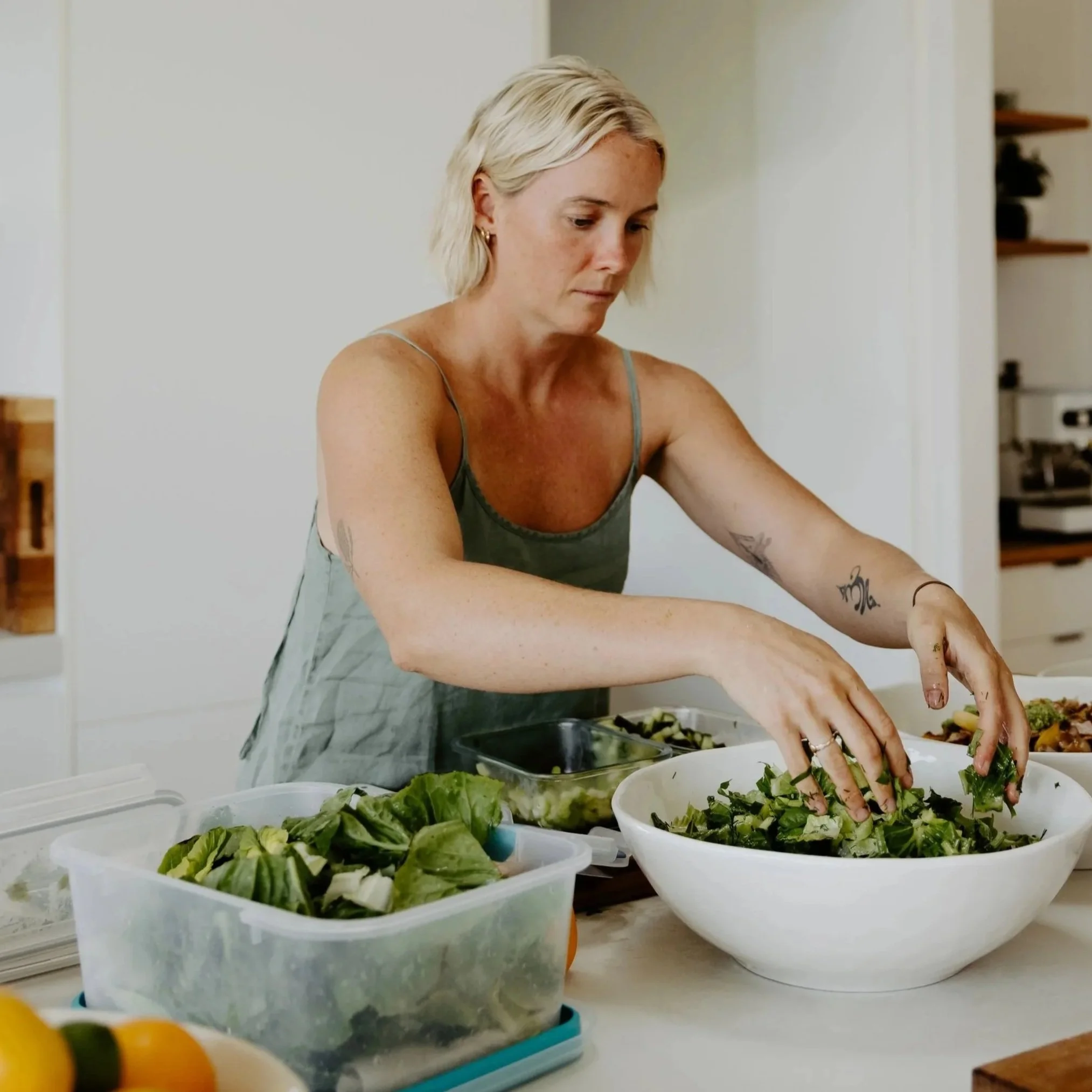 A woman preparing salads with a variety of fresh greens in large bowls on a kitchen counter.