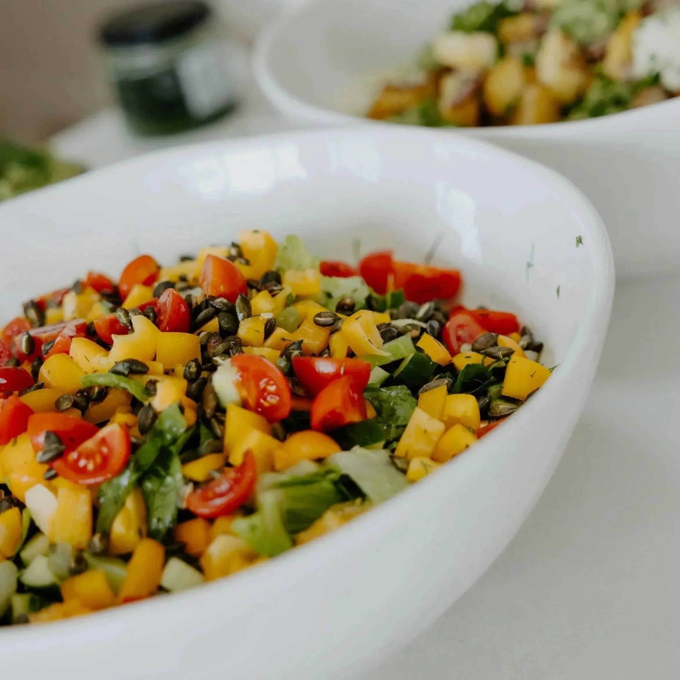 Close-up of a white plate with a colorful vegetable salad containing cherry tomatoes, yellow bell peppers, corn, and leafy greens.
